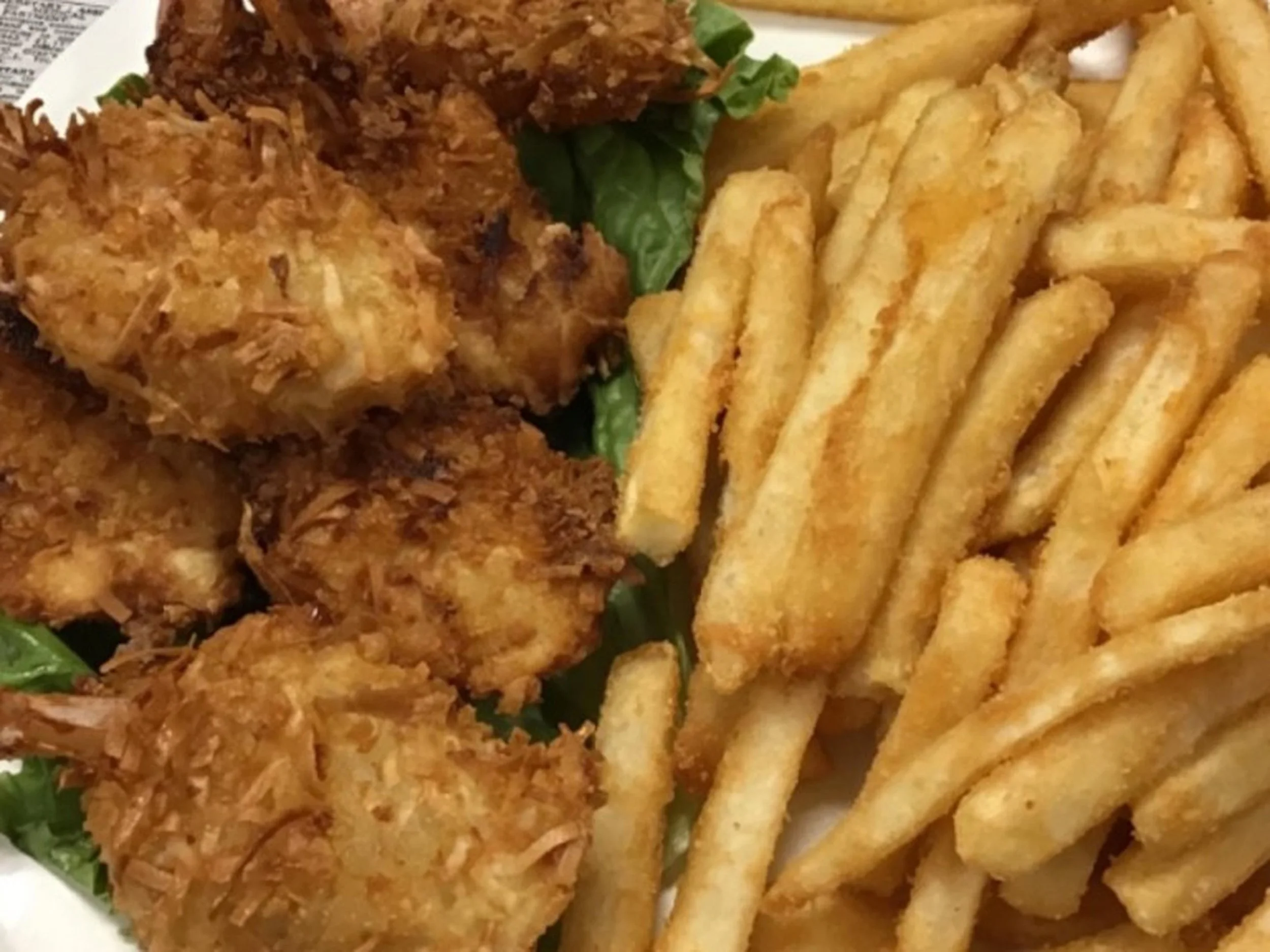 Fried chicken pieces, seasoned French fries, and some leafy greens on a white plate.