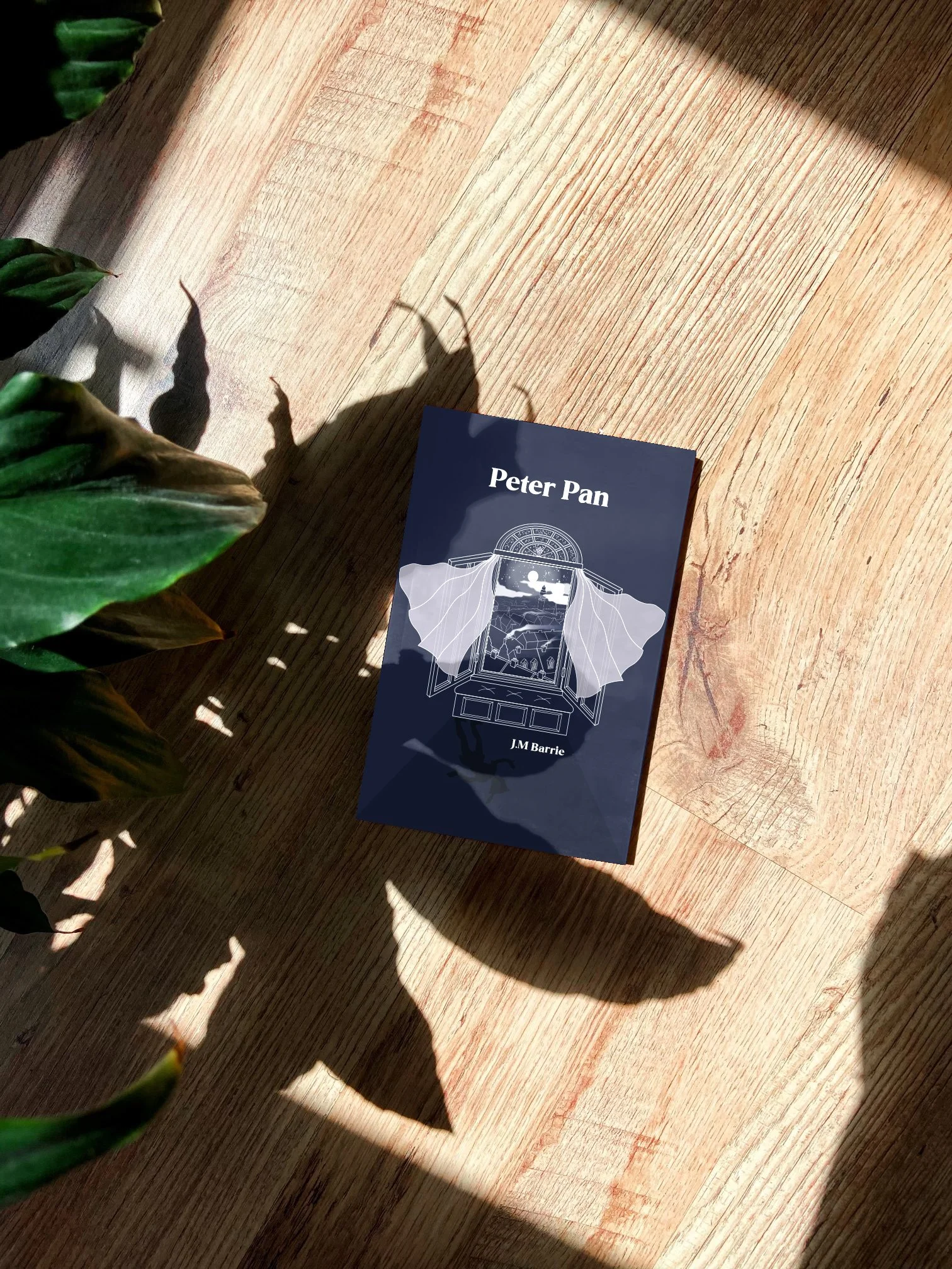 An alternative book cover design for J.M Barrie's Peter Pan based on wood block Lino printing. It is a navy background with an open window centred in the middle of the covered. You can see a starry London and Peter Pan's shadow at nighttime