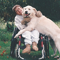 Person in wheelchair smiling with a golden retriever puppy outdoors