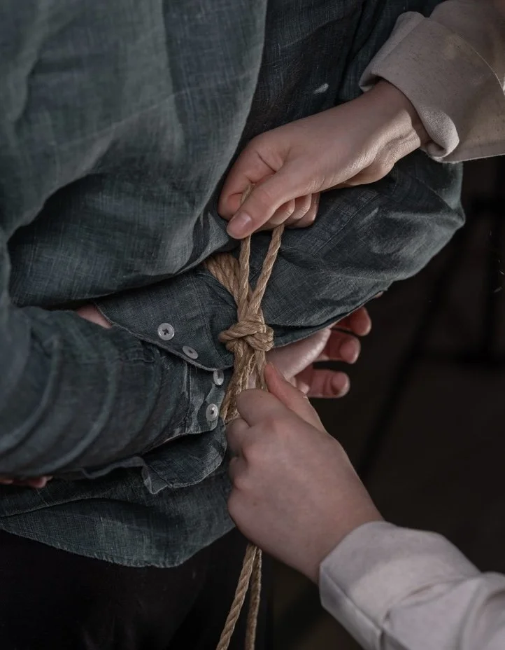 a person are tying a rope around another person's wrists