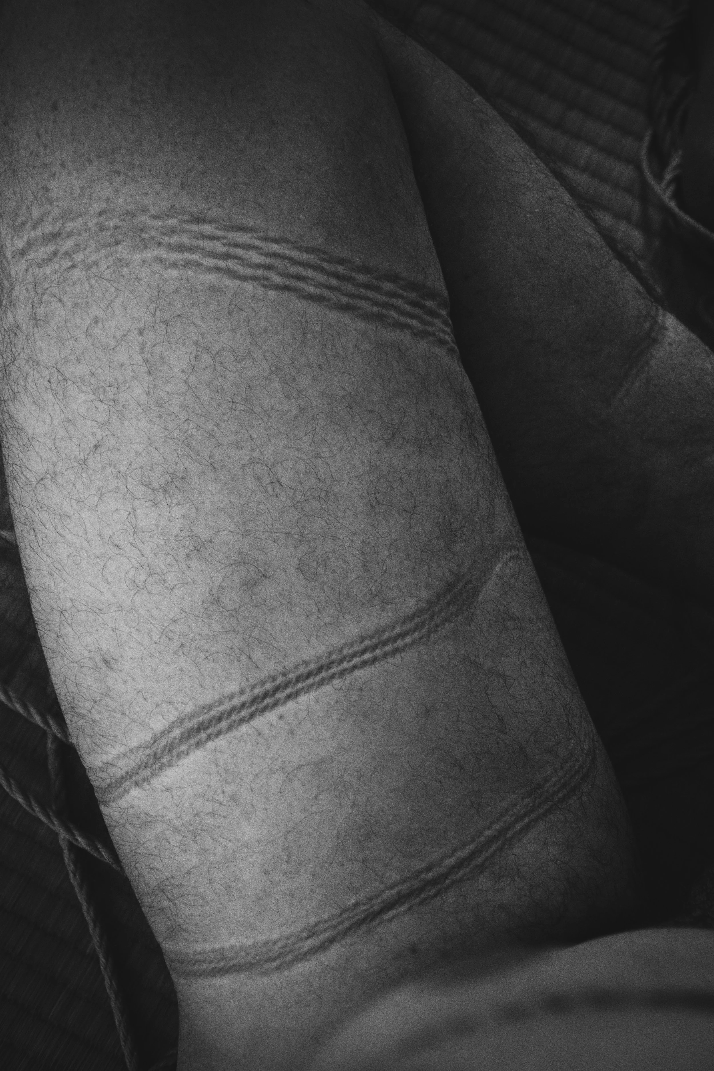 Close-up black-and-white photo of a person's legs, wearing shorts and a pair of sneakers, with visible hair on the legs.