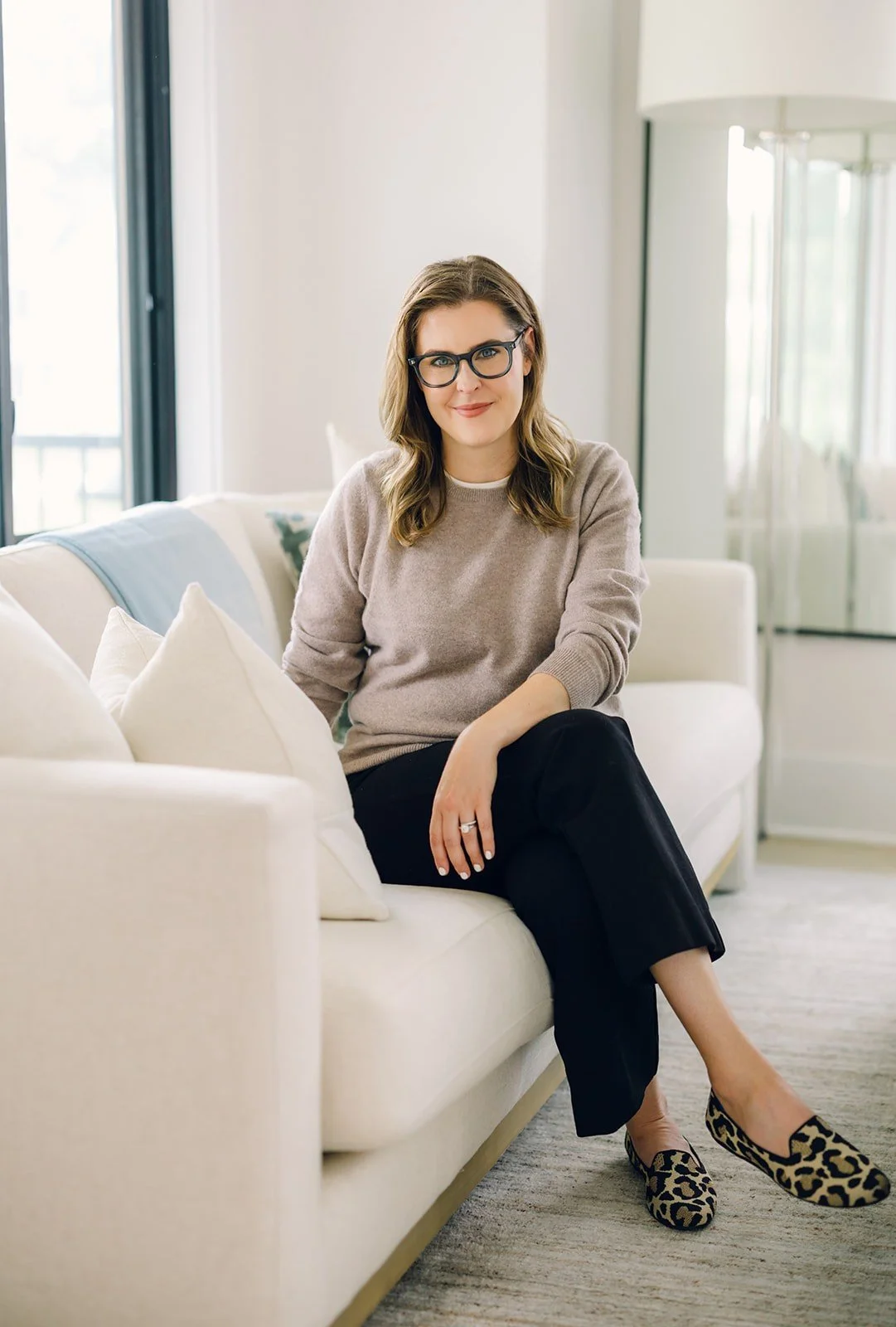 Virtual therapist for Virginia residents Claire Connolly, LICSW sits cross-legged on a cream couch, smiling.