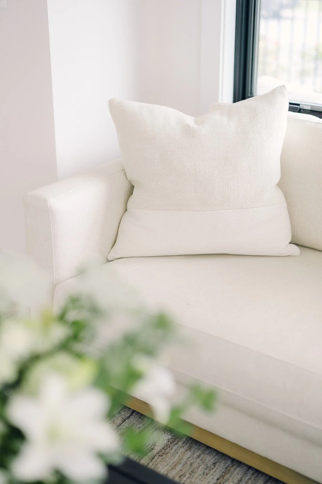 A light-colored couch and pillow with flowers in the foreground