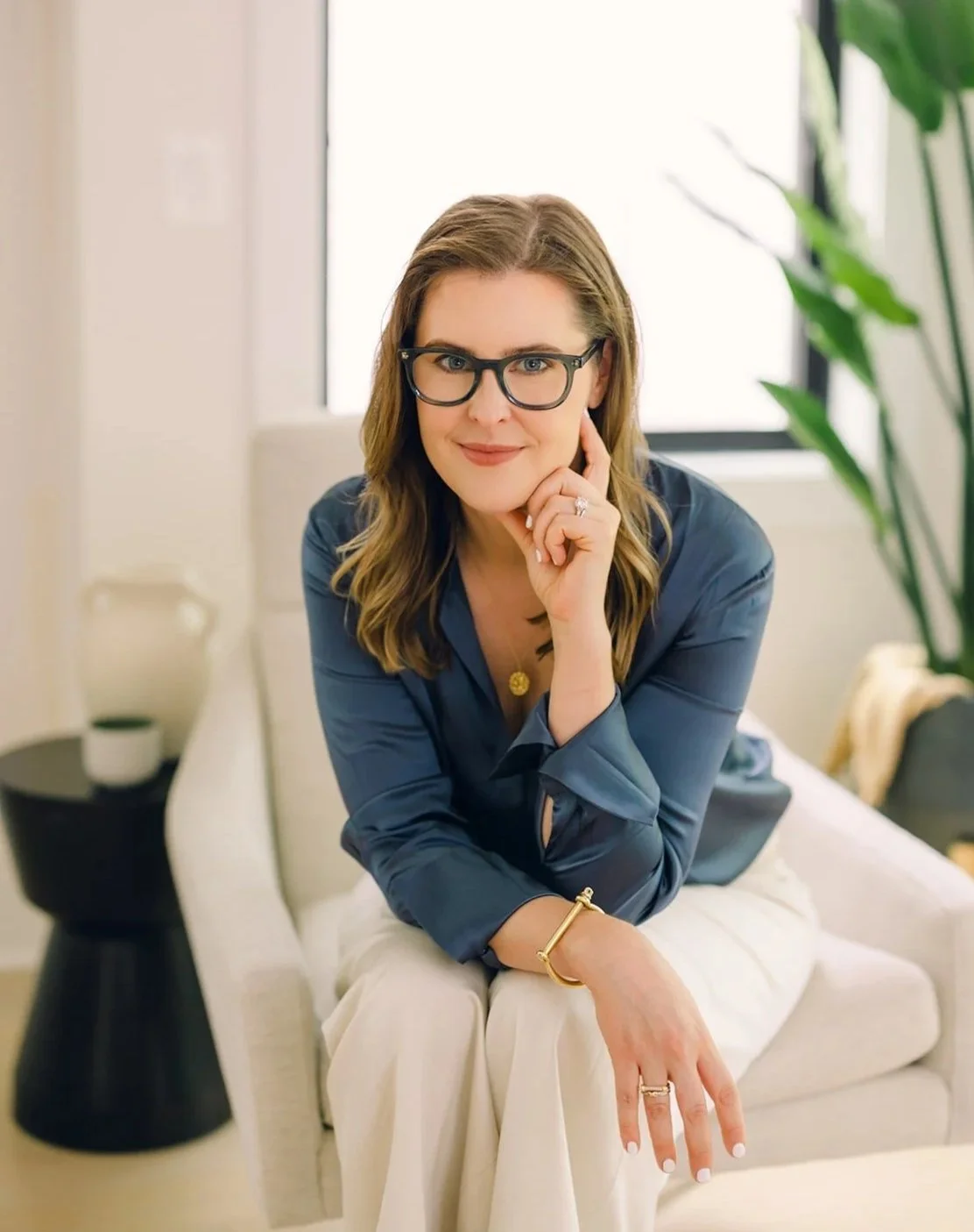 Claire Connolly, a virtual therapist in Virginia, smiling in a blue blouse, seated in a bright room with soft, warm interior decor.