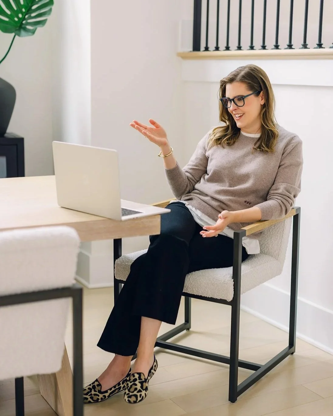 Claire Connolly gestures while speaking at a laptop in a bright room, representing a virtual therapy session with a client.