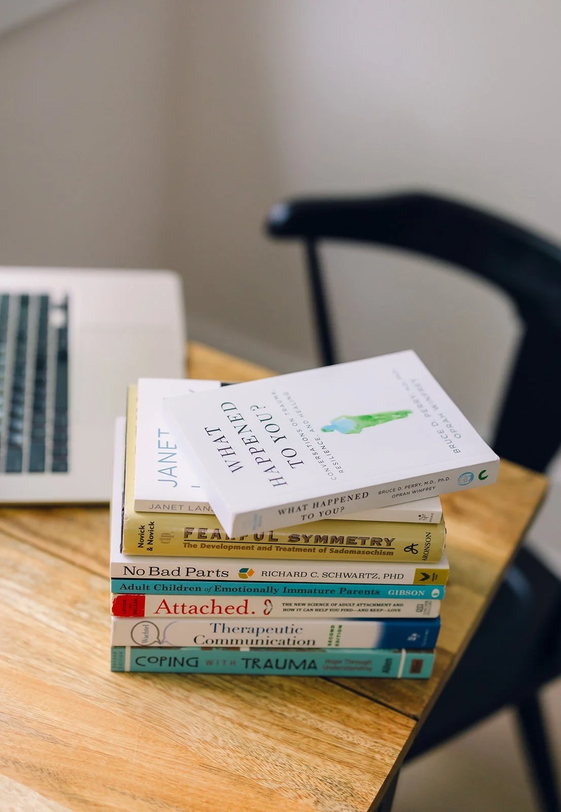A stack of therapy books on a desk, including "Attached," "No Bad Parts," and "What Happened to You?," reflecting a trauma-informed practice.