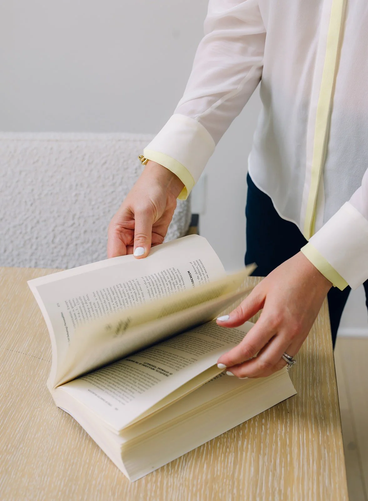 Person flipping pages in a large open book on a light wooden table.