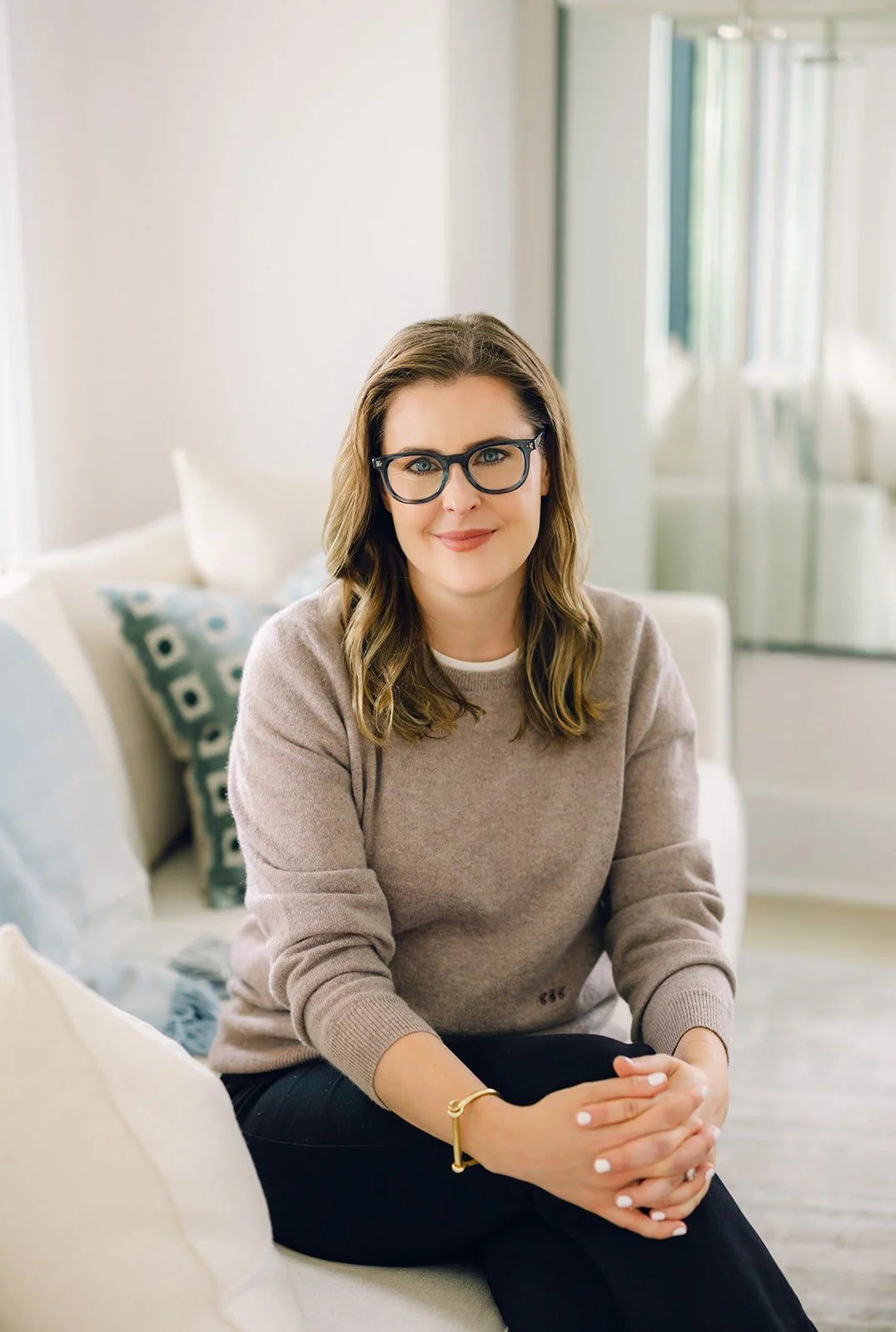 DC-based couples therapist Claire Connolly, LICSW sits smiling on a cream sofa with blue pillows in a well-lit room.
