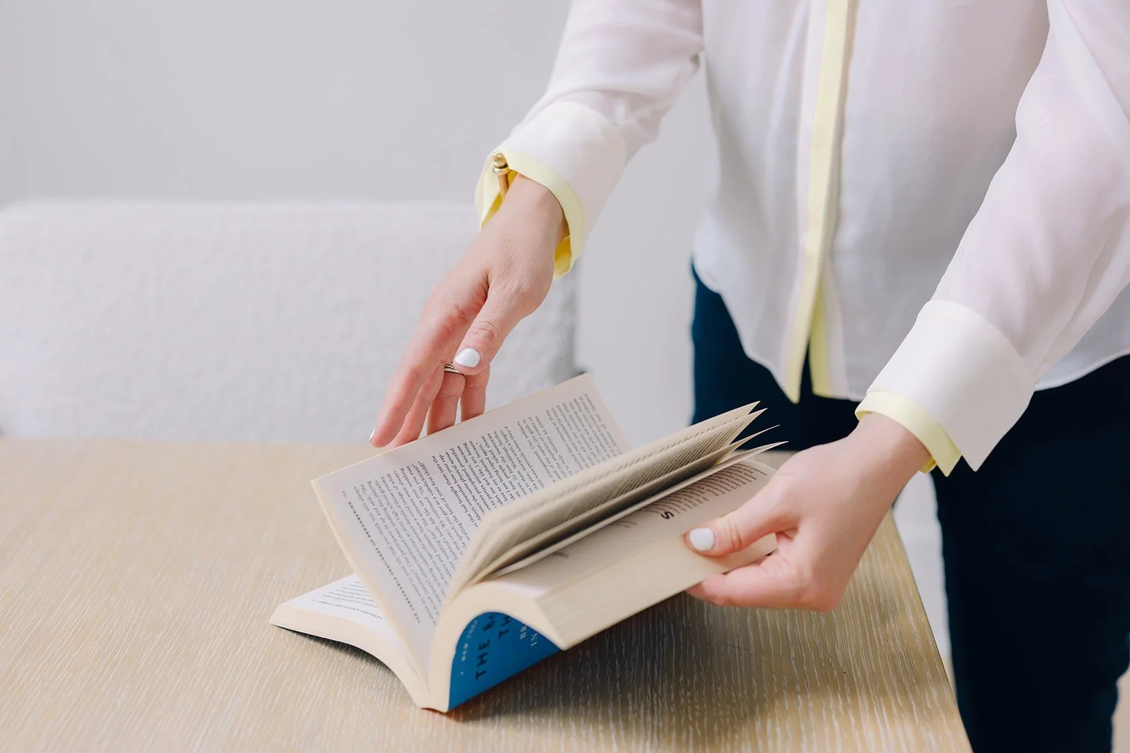 Person in a white shirt flipping through the pages of a large book on a wooden table.