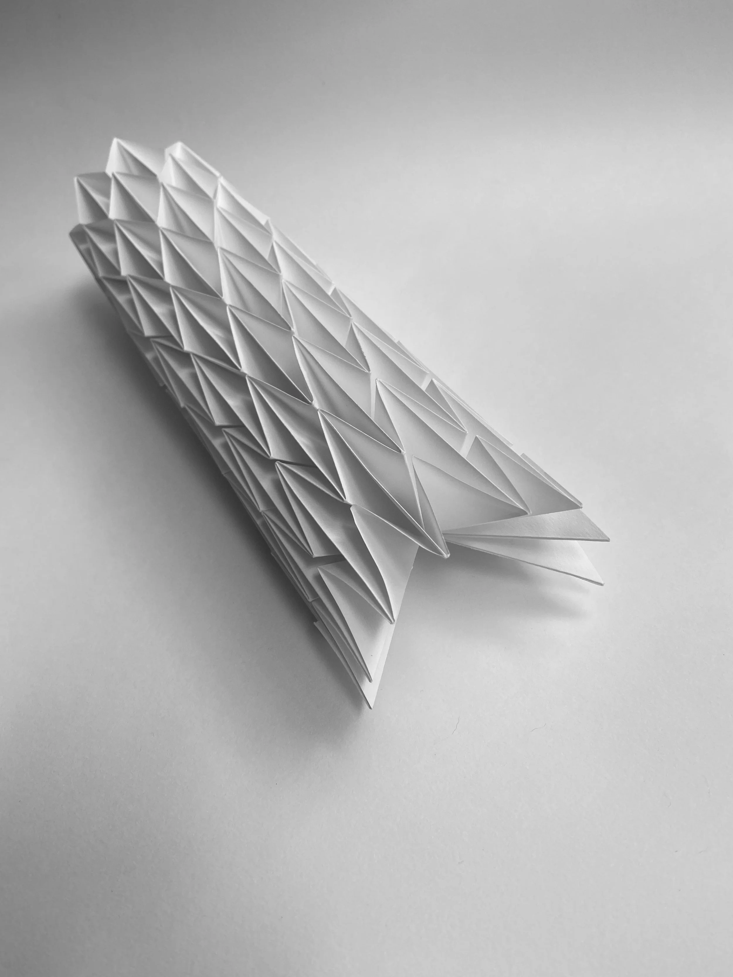 A folded paper sculpture with a geometric, honeycomb pattern resting on a plain surface.