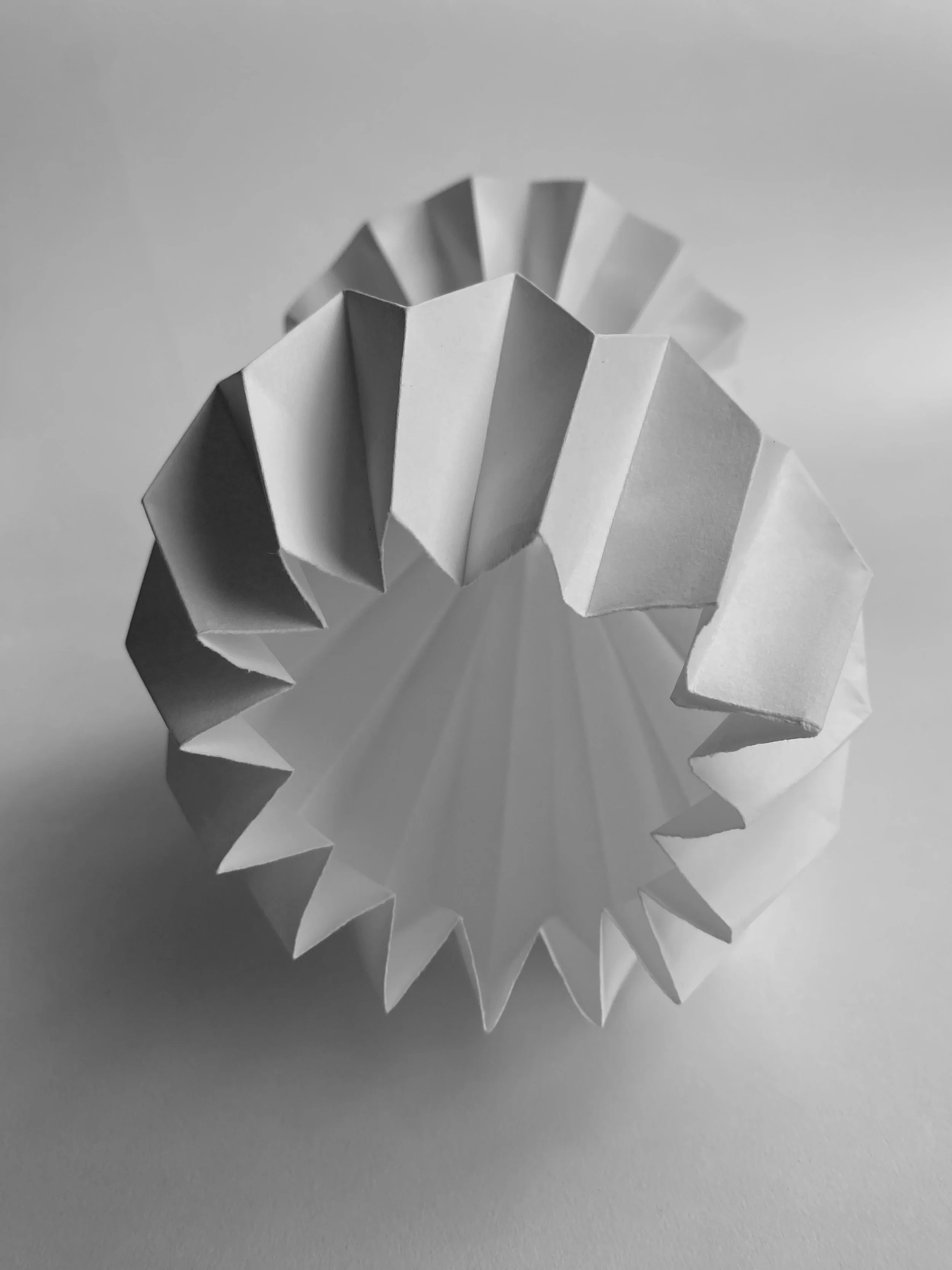 Close-up of a white paper chain with folded edges, on a gray background, in black and white.