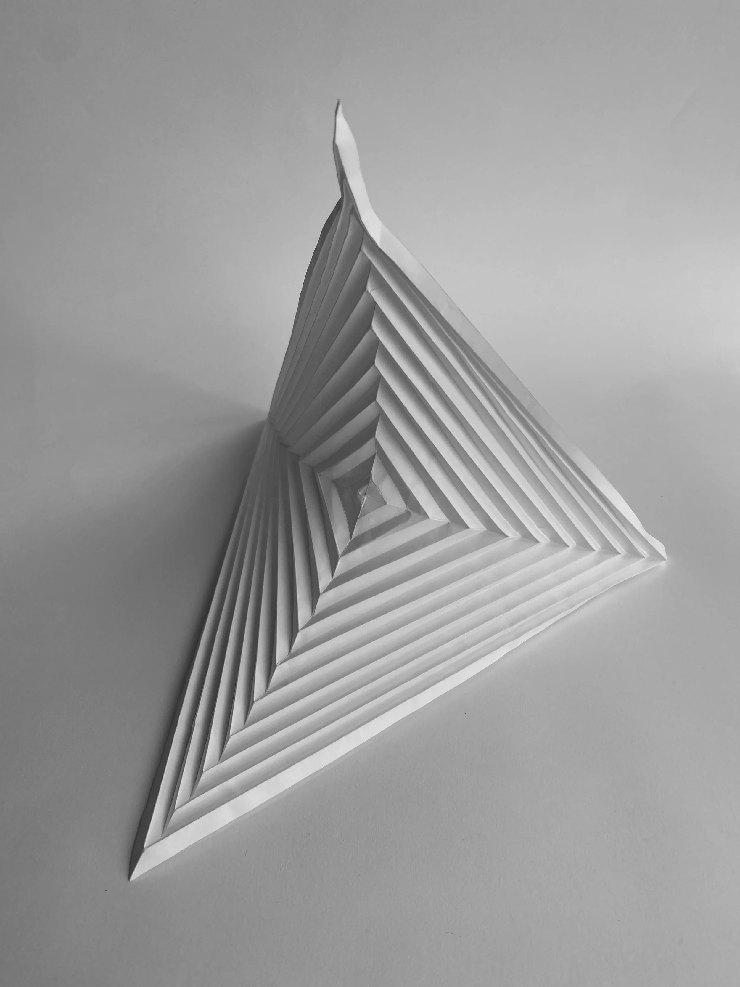 A white paper origami boat with layered, geometric edges, set against a plain gray background.