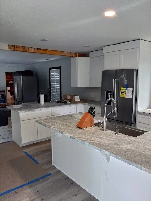 Modern kitchen with white cabinets, granite countertops, stainless steel refrigerator, and a double sink with a high-arc faucet.