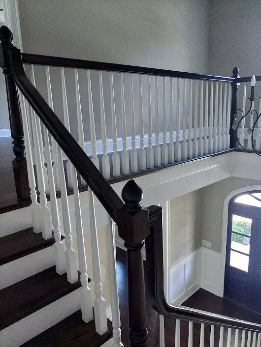 Inside view of a staircase with dark wood handrails and white balusters, leading to a lower level with a curved black door and a window.
