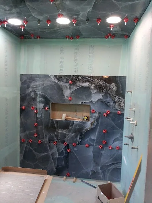 Construction room with navy blue marble-patterned wall, small recessed shelf, and numerous red screw anchors on the wall and ceiling.