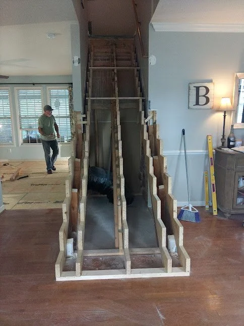 Construction of a staircase in a home, with visible framework and two metal slides for stairs, surrounded by tools and furniture.