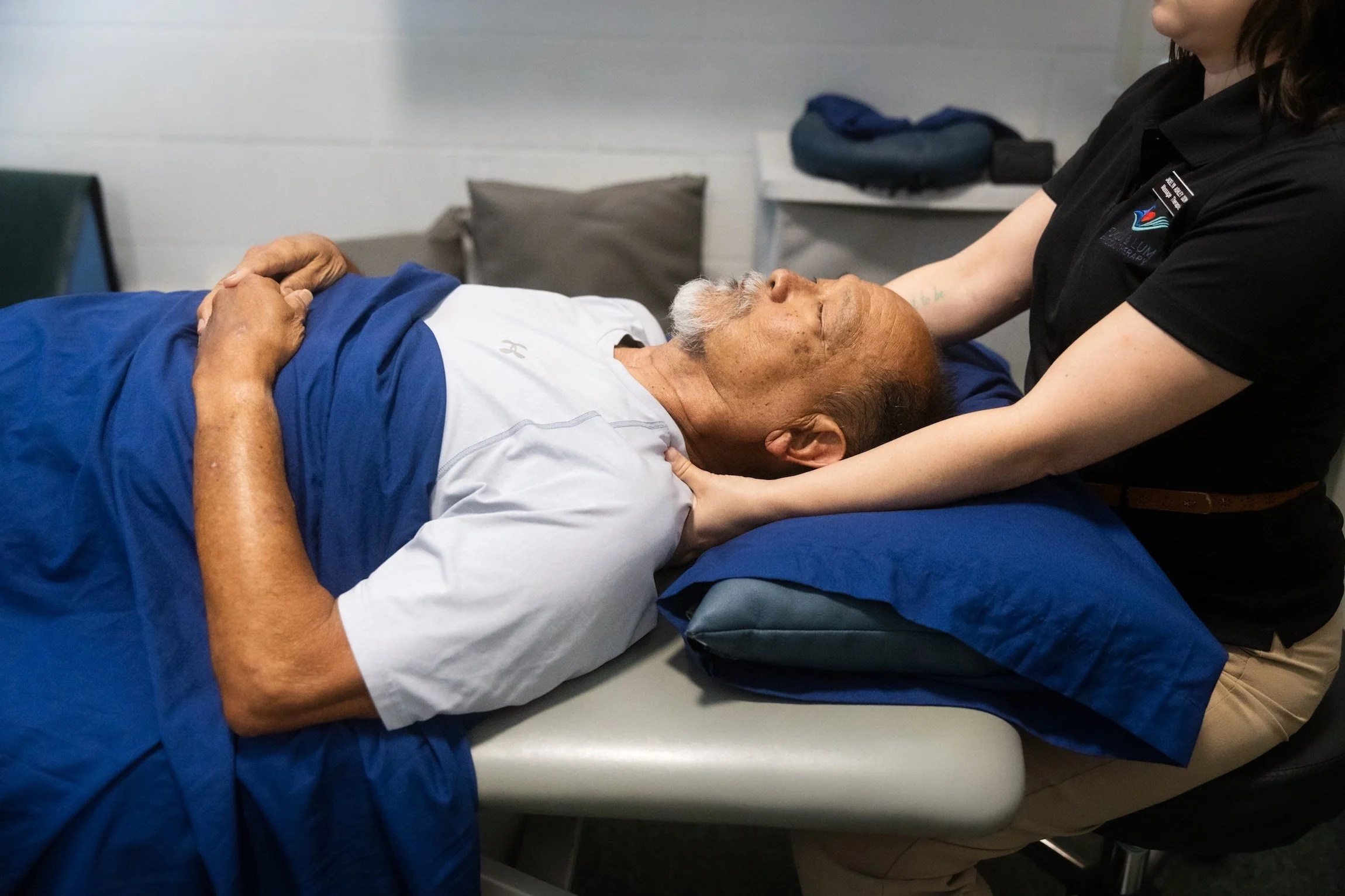 A licensed massage therapist performs therapeutic massage on a patient's shoulder.