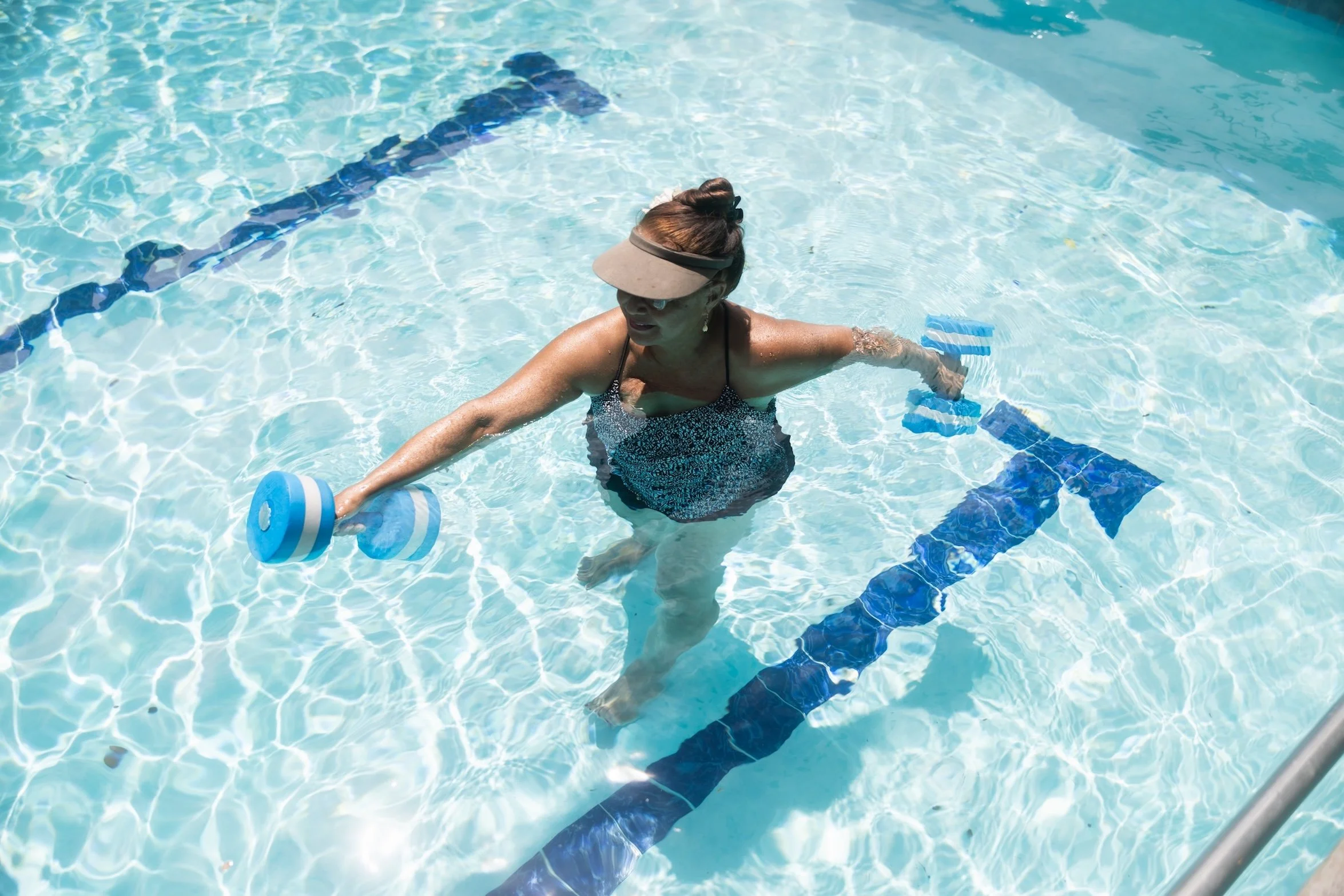 A patient performs a standing arm exercise with water dumbbells in the therapy pool.