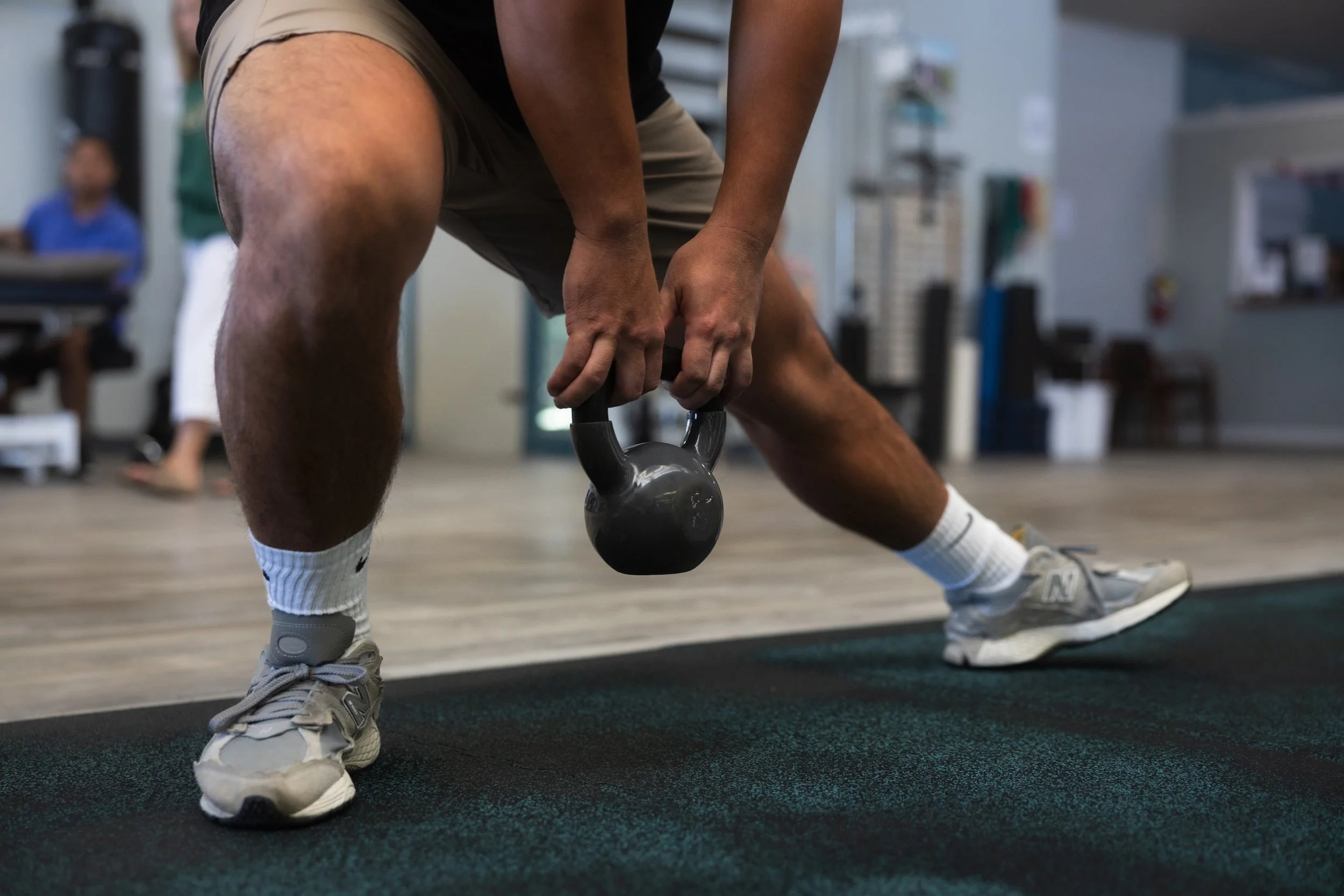 A patient practices safe lifting mechanics with a kettlebell during occupational rehab at Fukuji & Lum's W.O.R.C. center."