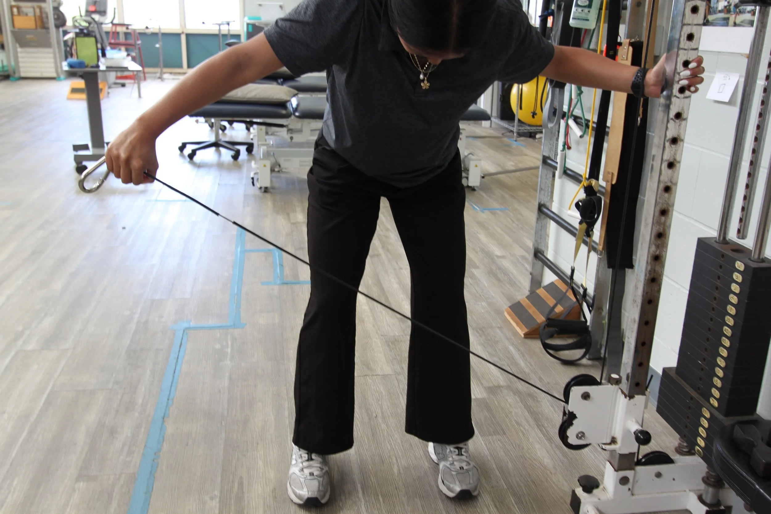 A patient performs a resisted pulling exercise on a cable column to rebuild strength during occupational rehab at Fukuji & Lum.