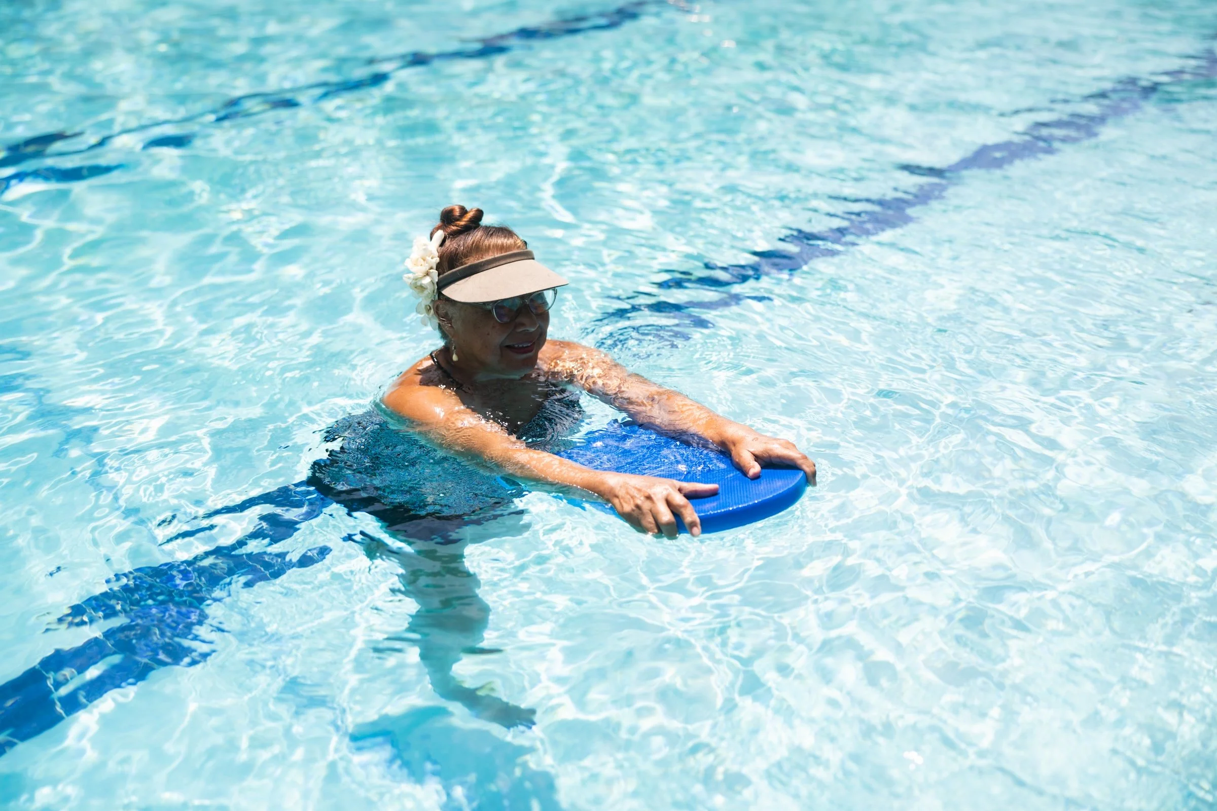 An older adult floats with a kickboard during a relaxed aquatic therapy session.