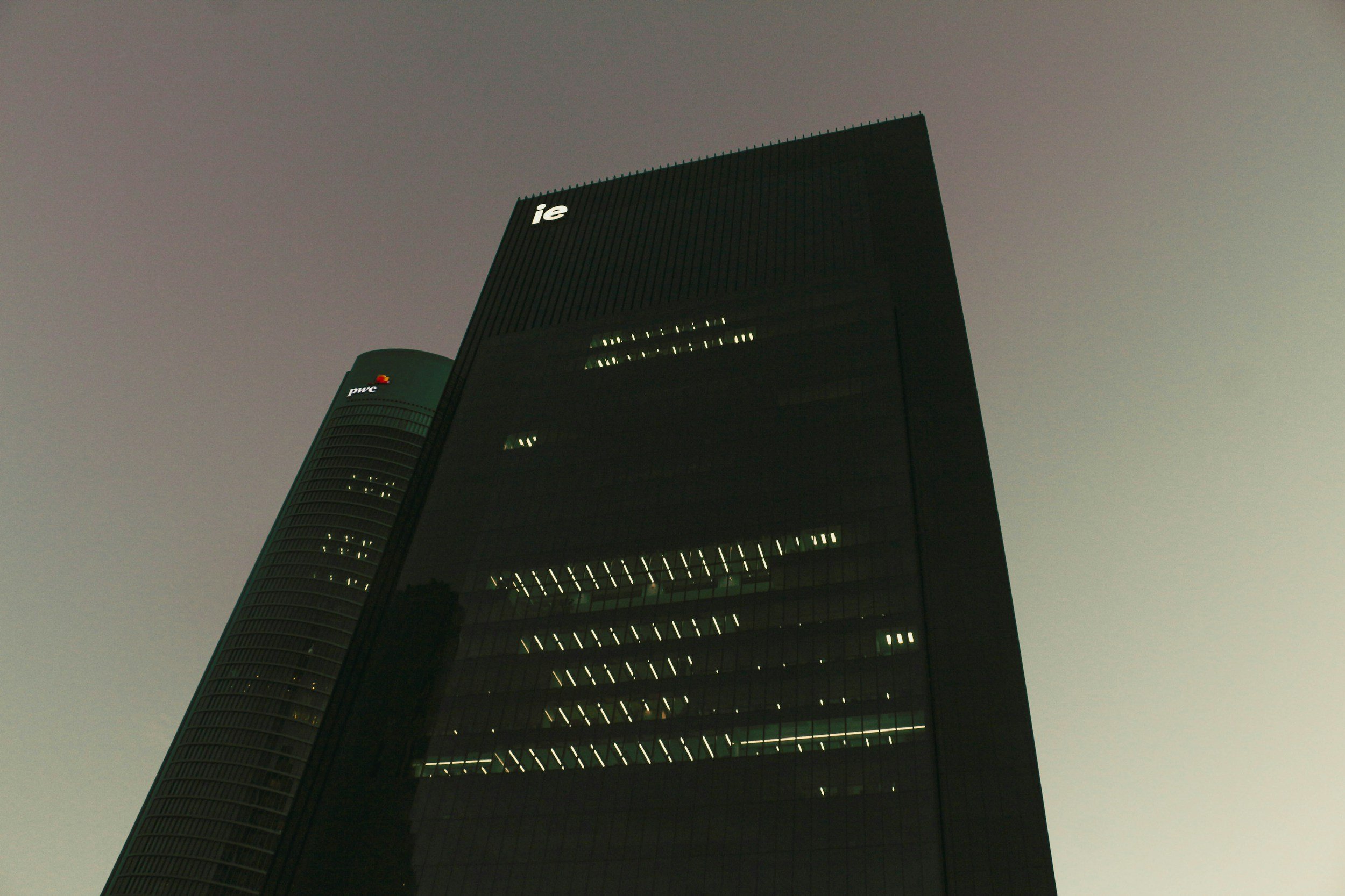 Dark skyscraper with illuminated windows and company logos for PwC and an unclear logo near the top