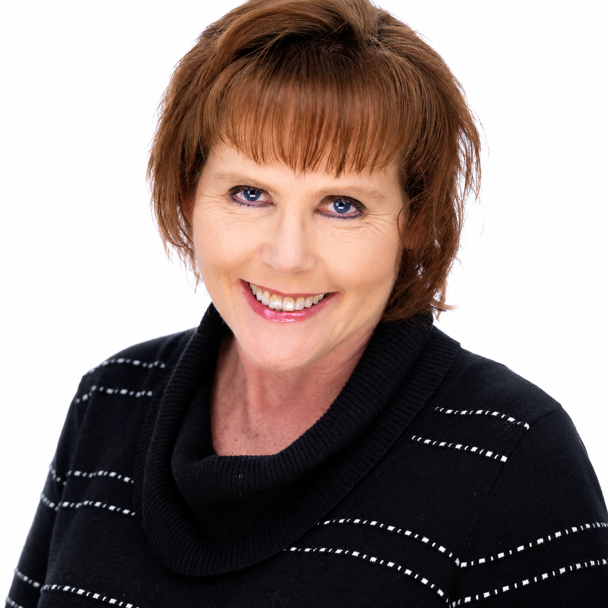 A woman with short red hair, blue eyes, and a black striped turtleneck sweater, smiling at the camera against a white background.