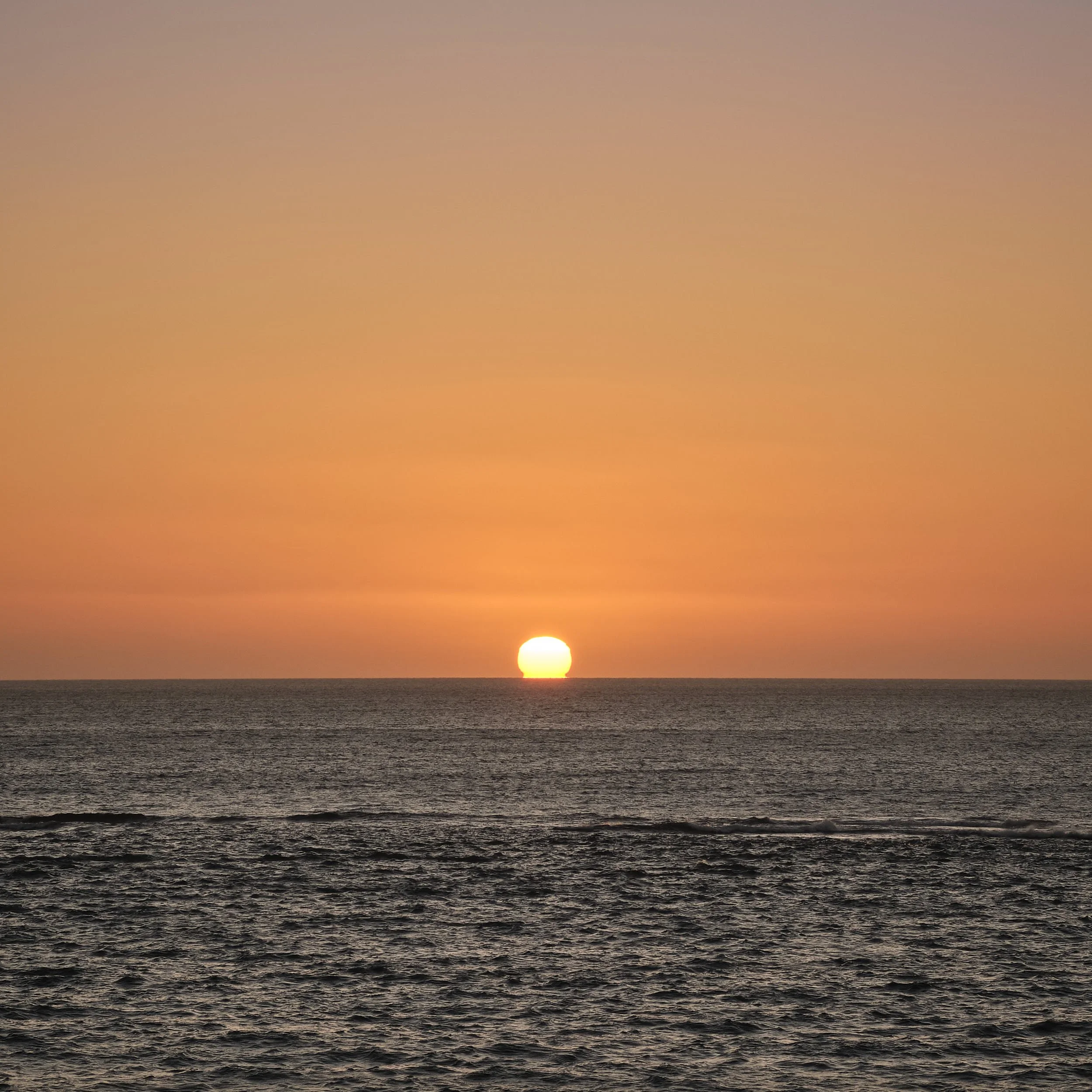 Das Bild zeigt einen Sonnenuntergang mit orangenem Himmel und einer Sonne die ins dunkelblaue Meer eintaucht.