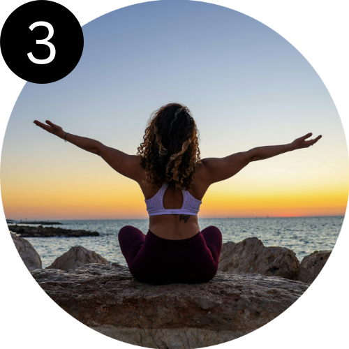 Woman practicing yoga on rocks by the water at sunset