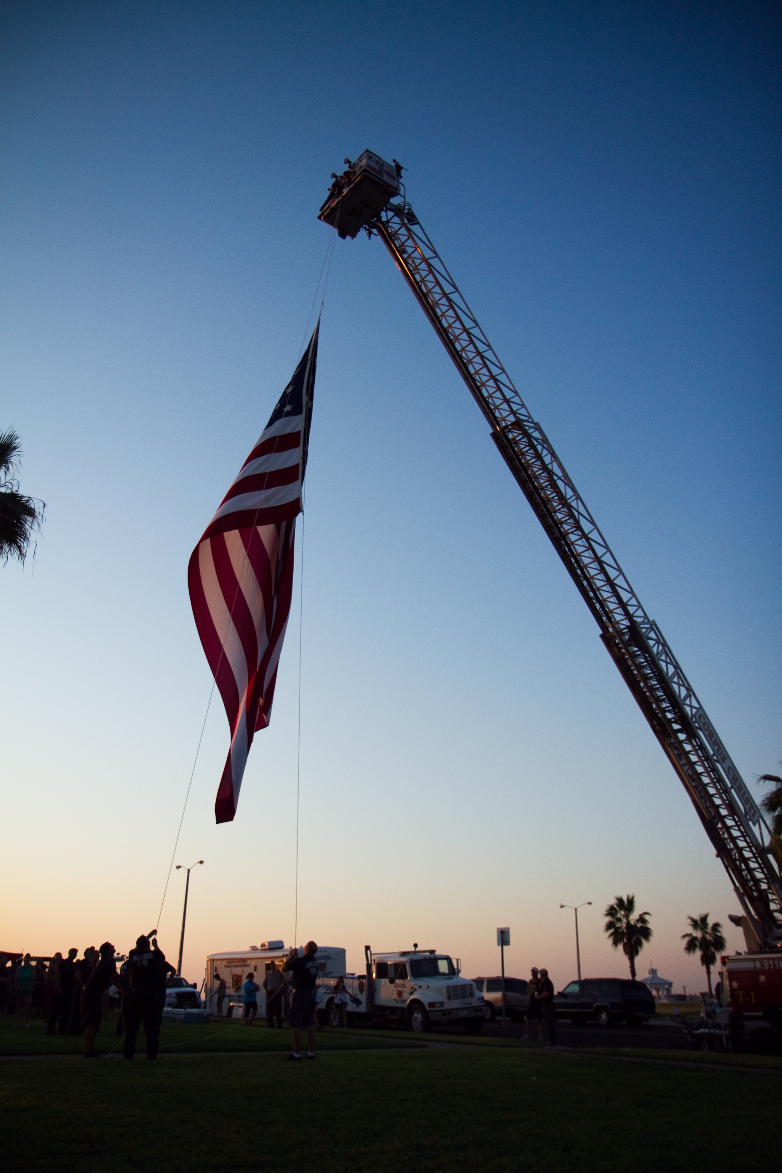 People gathered outdoors during sunset, with fire truck ladder extended, holding an American flag.