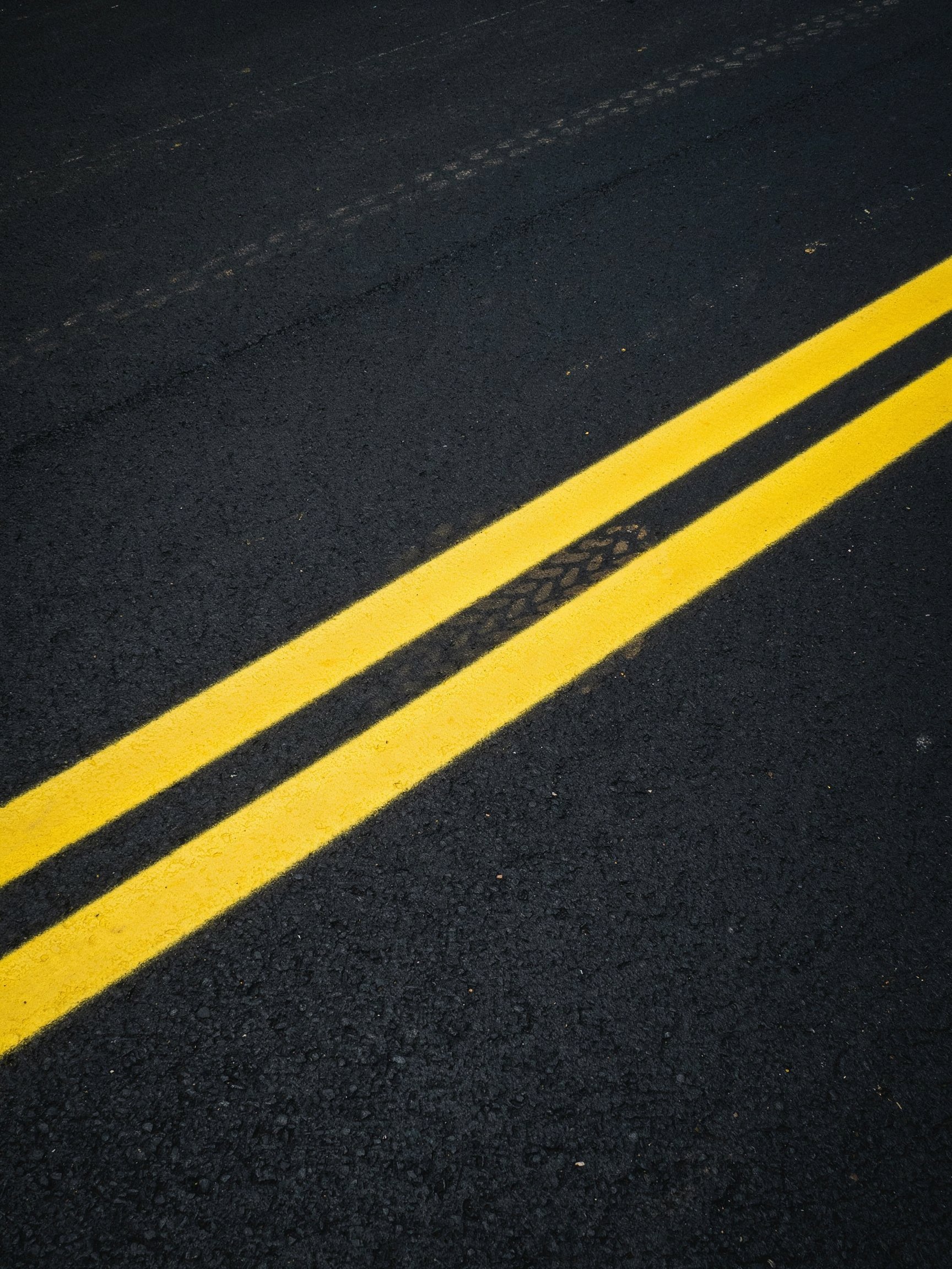 Close-up of a section of freshly painted yellow double lines on black asphalt pavement at night.