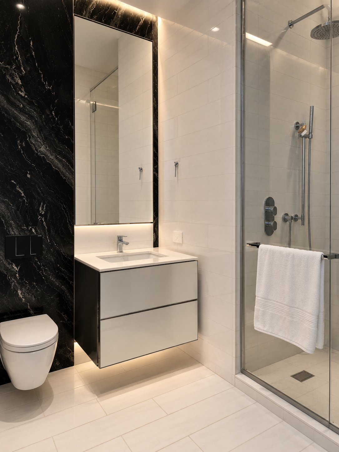 Modern bathroom with black and white marble and tile designs, a large mirror, a floating vanity with a sink, a wall-mounted toilet, and a glass-enclosed shower with a towel hanging on the door.