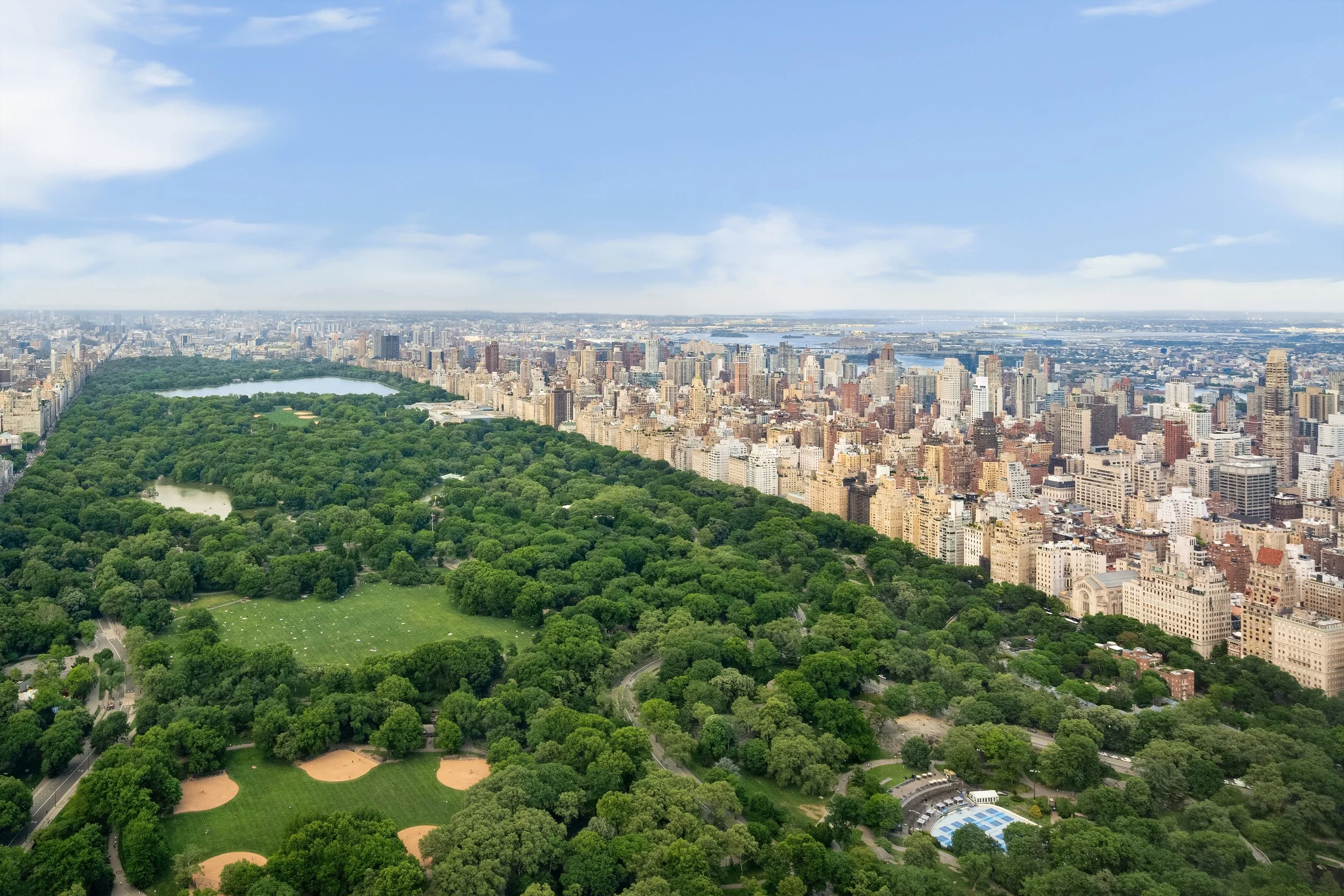 Aerial view of Central Park in New York City with surrounding high-rise buildings, water bodies, and a partly cloudy sky.