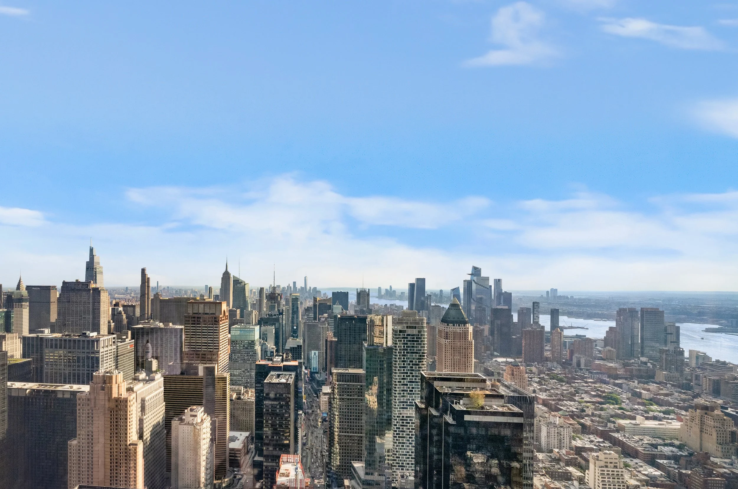 A city skyline with numerous tall skyscrapers under a bright blue sky with scattered clouds.