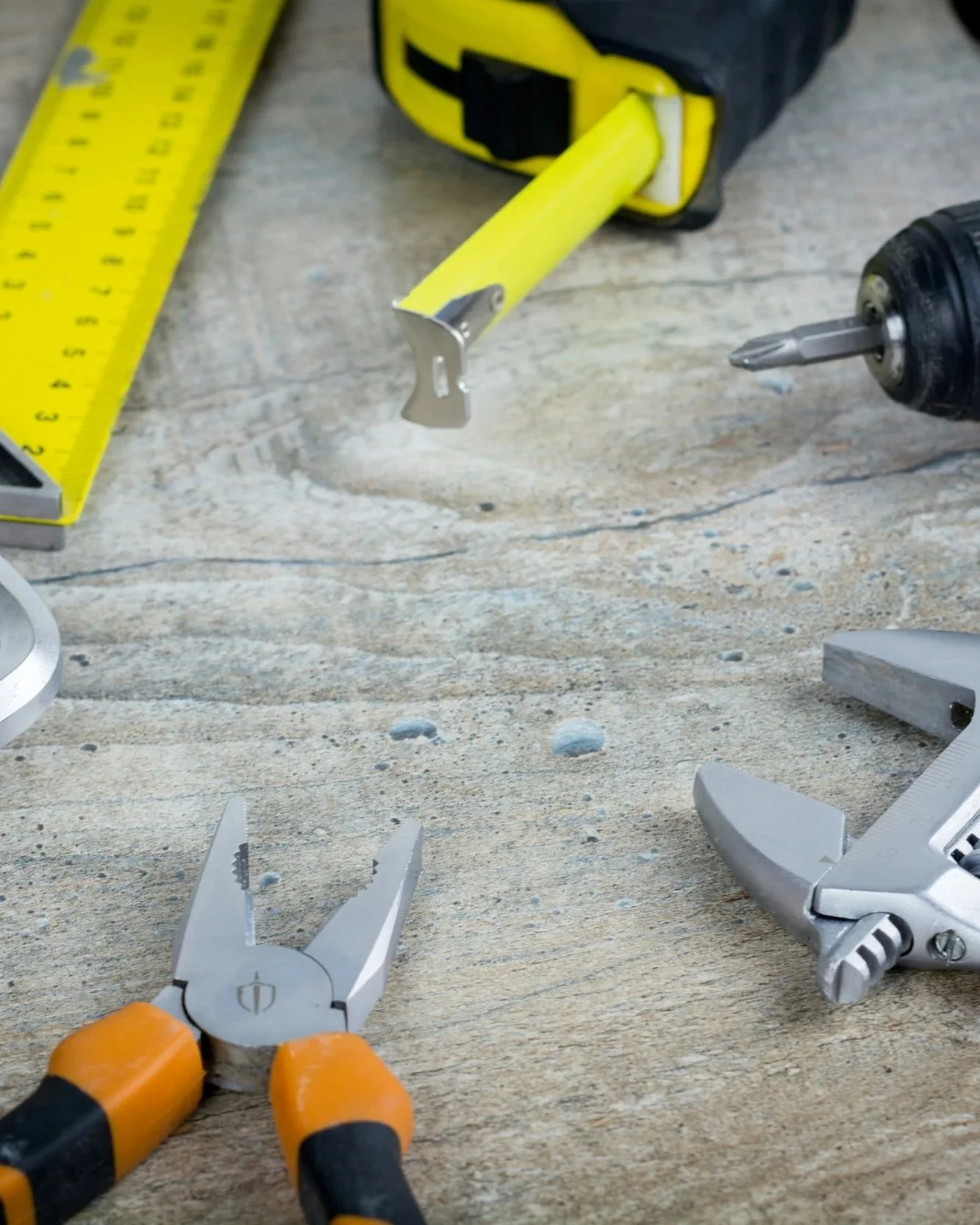 Outils de réparation ou de bricolage, dont une pince coupante, un tournevis, un cutter et un perceuse, posés sur une surface en bois, avec une règle en métal jaune à gauche.