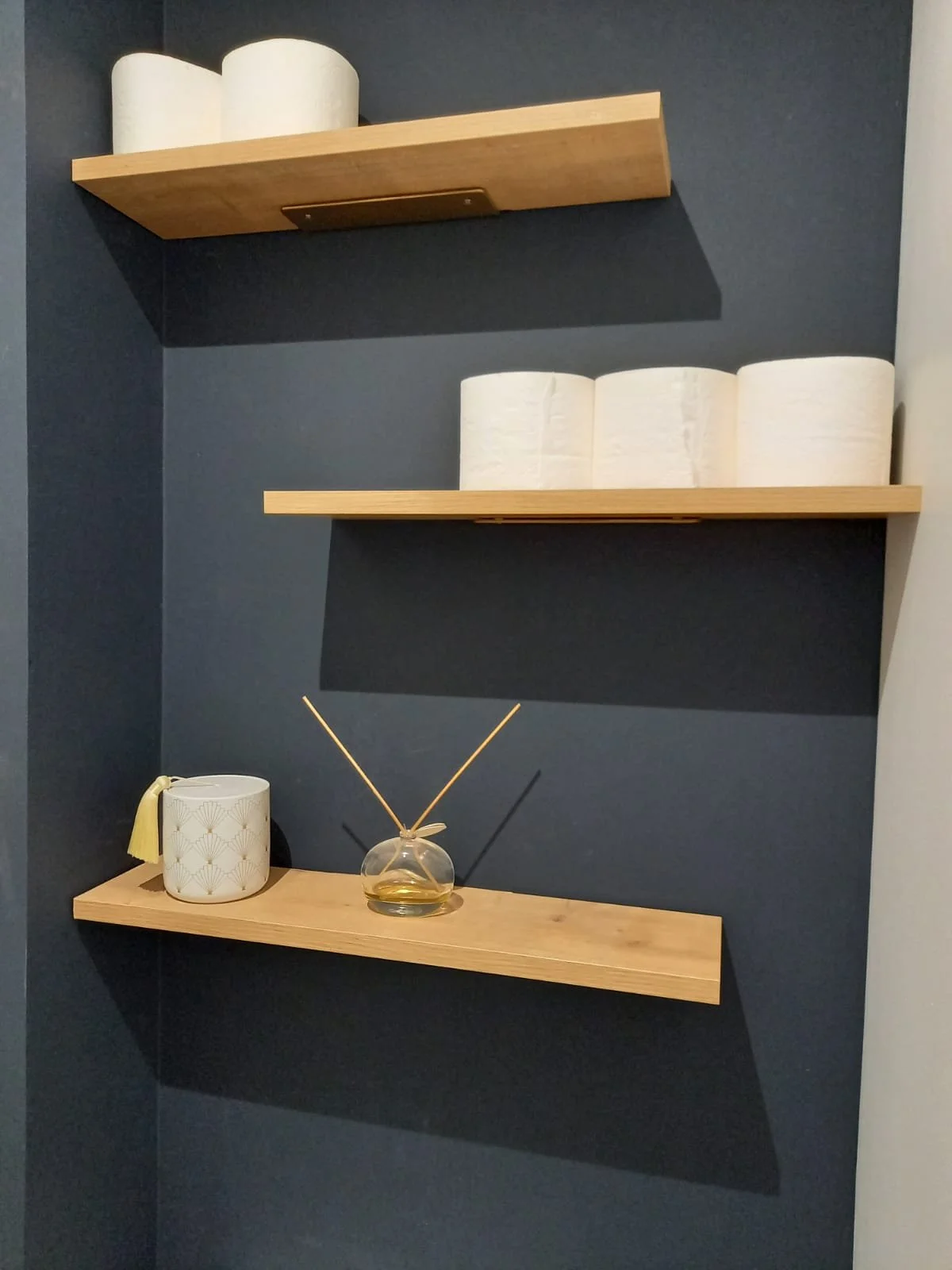 Trois étagères en bois fixées à un mur gris foncé.