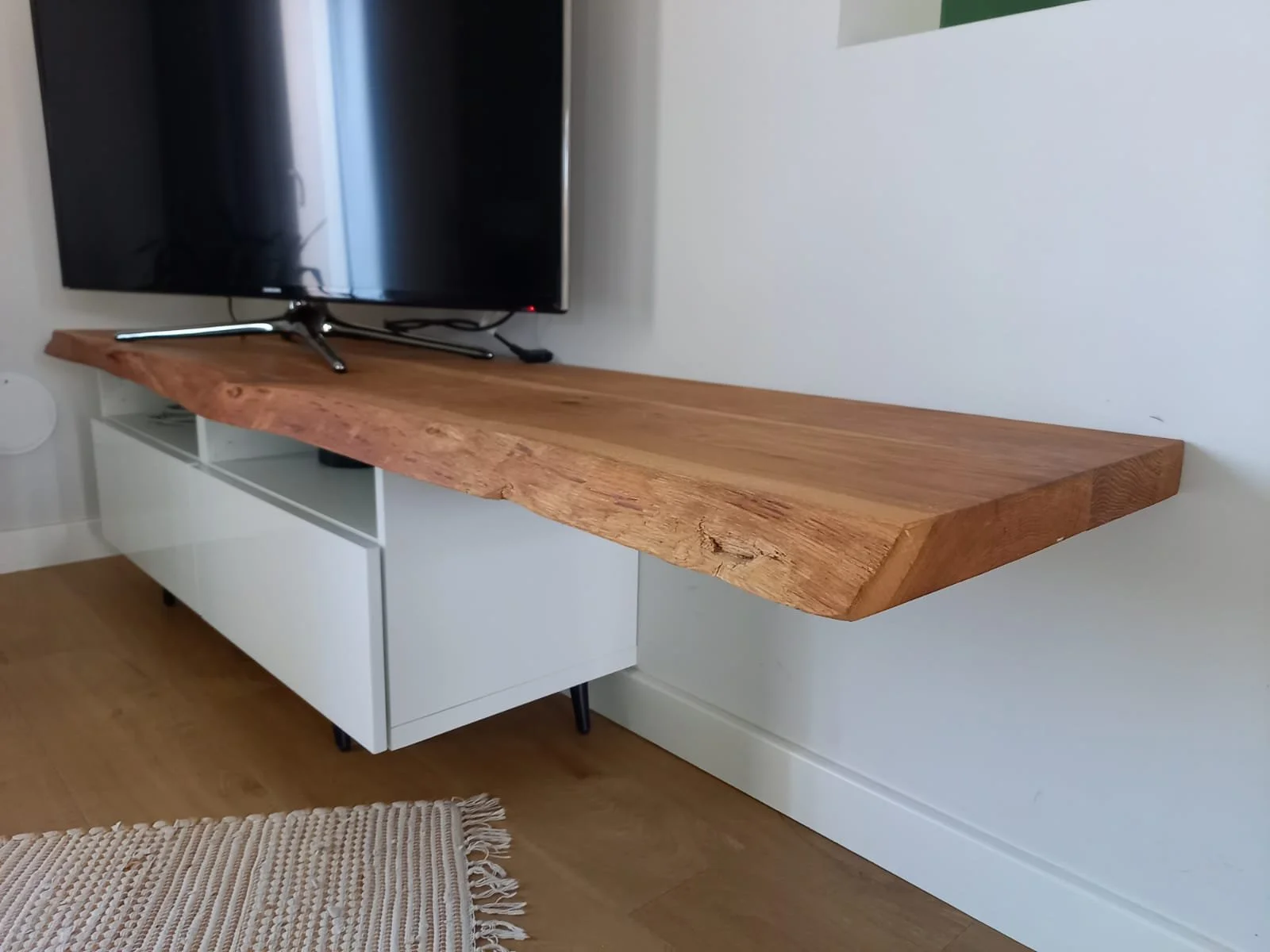 Une télévision posée sur un meuble en bois fixé au mur dans une pièce moderne.