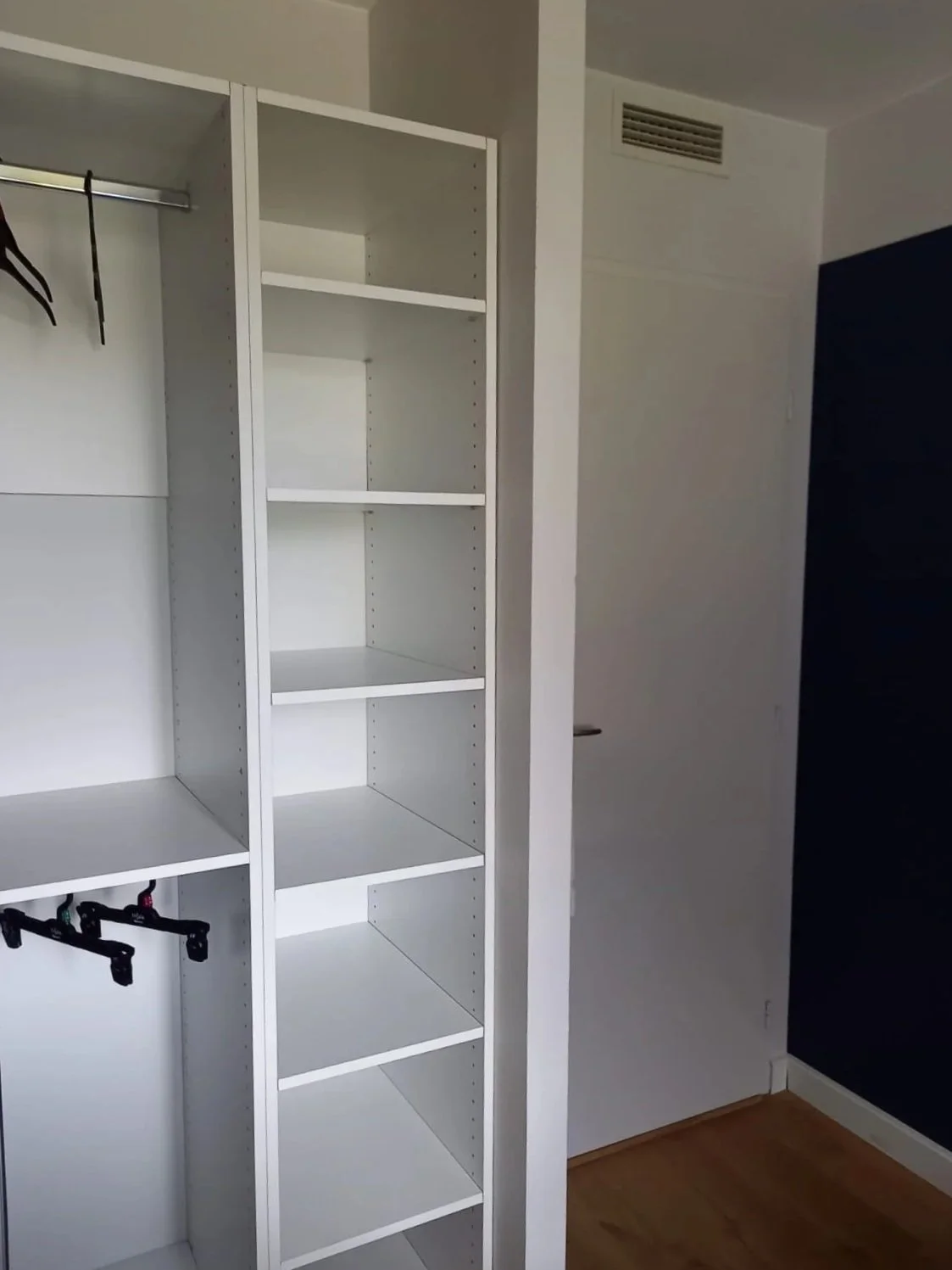Une armoire blanche vide avec plusieurs étagères, située dans une chambre.