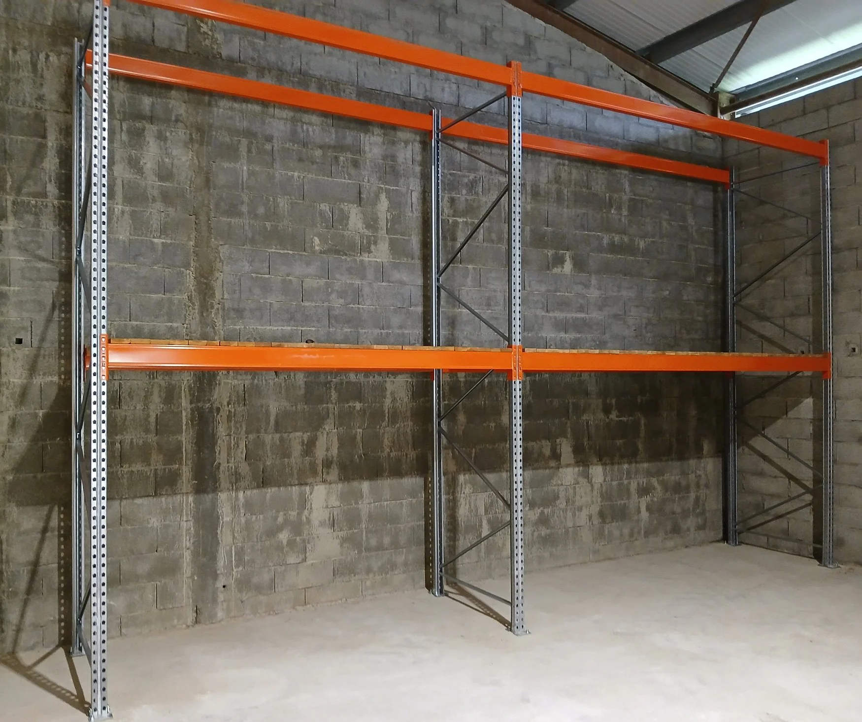 Une étagère métallique avec trois niveaux de rayonnages en bois orange dans une pièce avec un mur en briques grises et un plafond en métal.