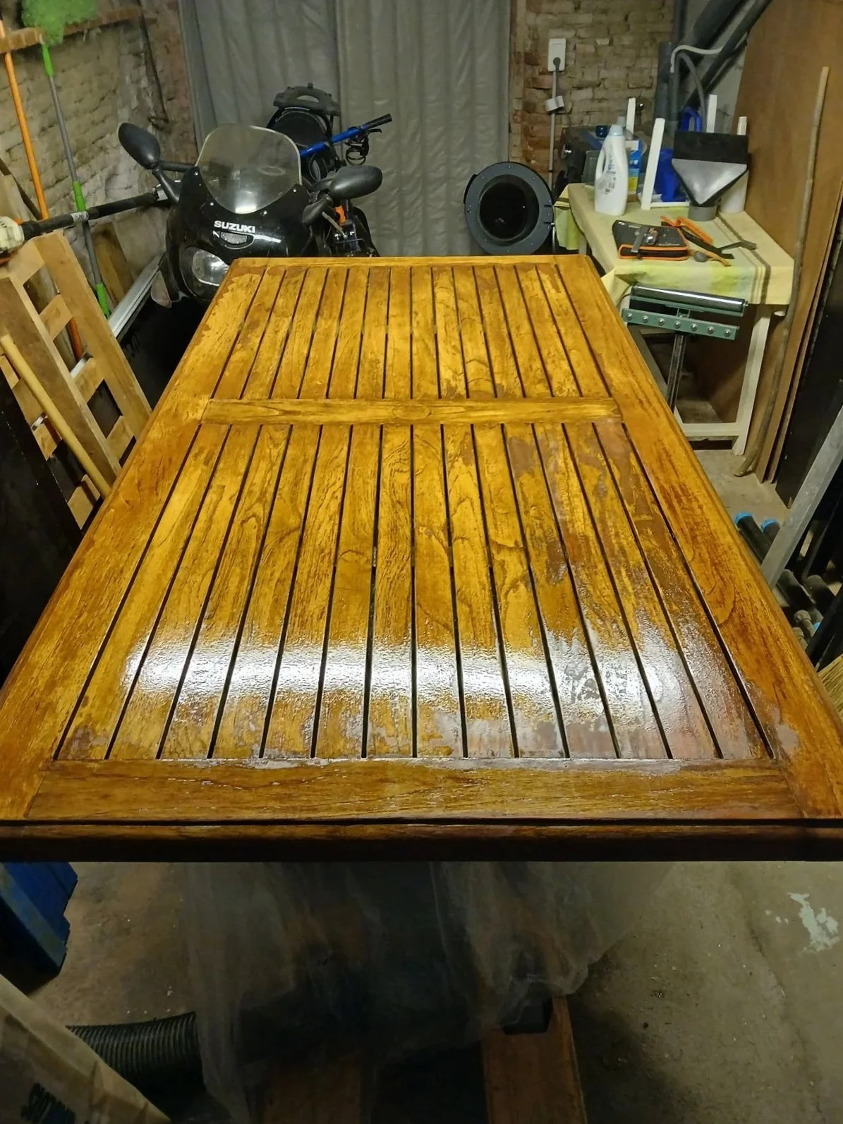 Table en bois verni dans un atelier, plusieurs outils, produits de nettoyage, et matériel de bricolage.