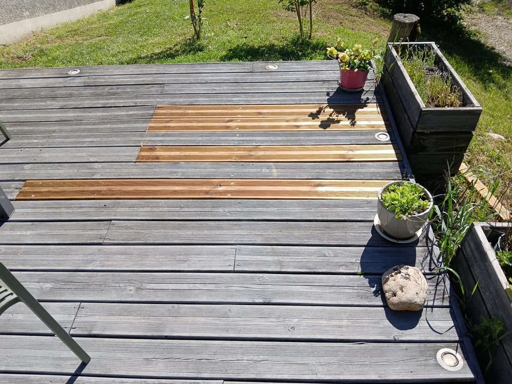 Une terrasse en bois avec des jardinières contenant des plantes, quelques plantes en pot et une pierre décorative.
