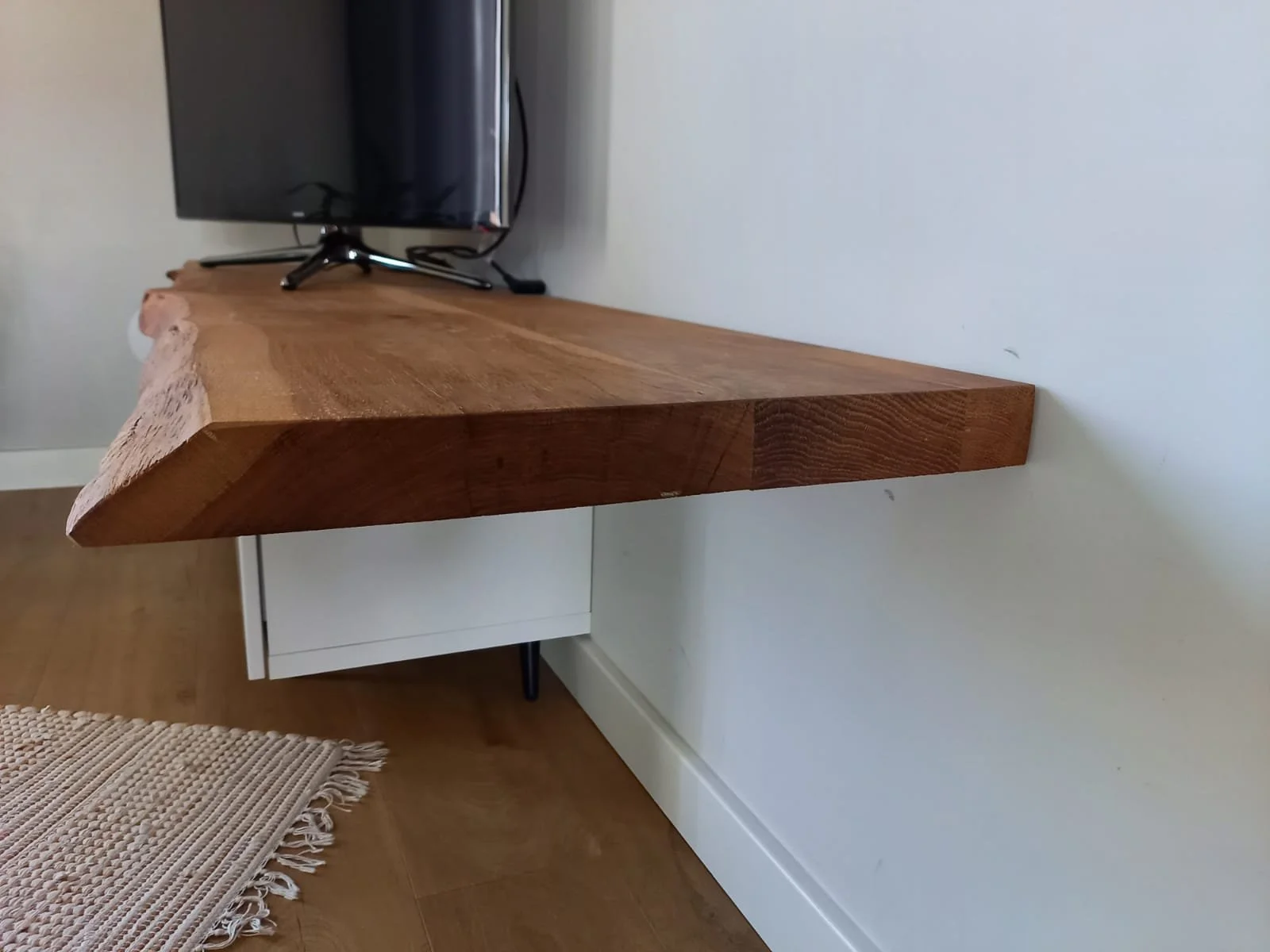 Une télévision sur un meuble en bois massif fixé à un mur blanc.