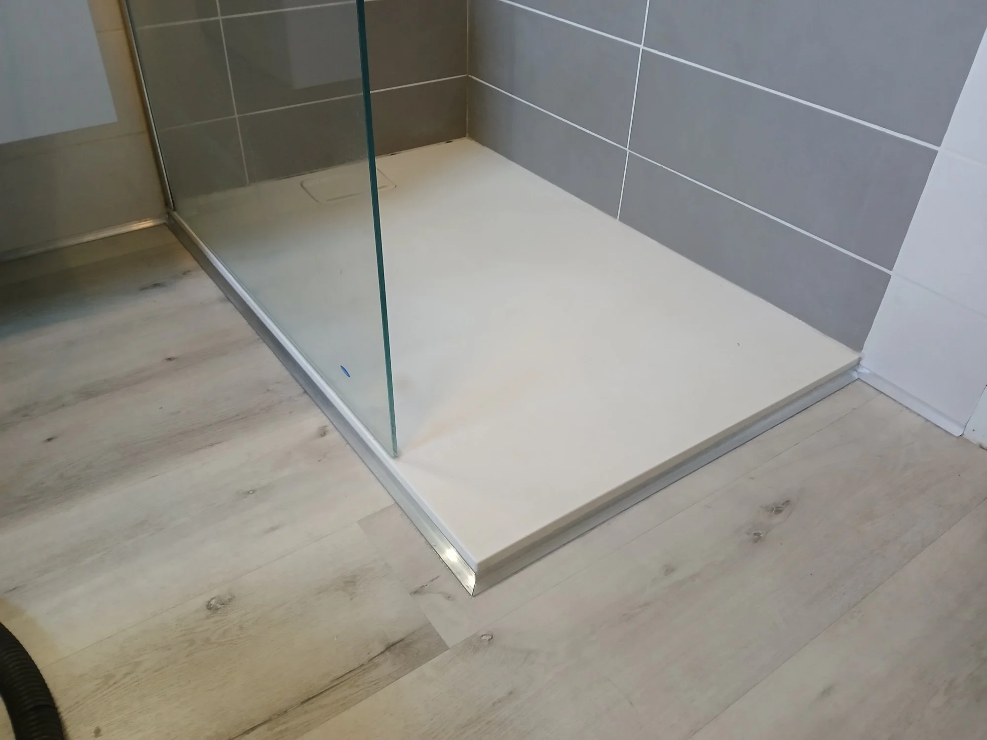 Une cabine de douche en verre avec des murs en carreaux gris et un sol en pierre blanche, dans une salle de bains moderne.