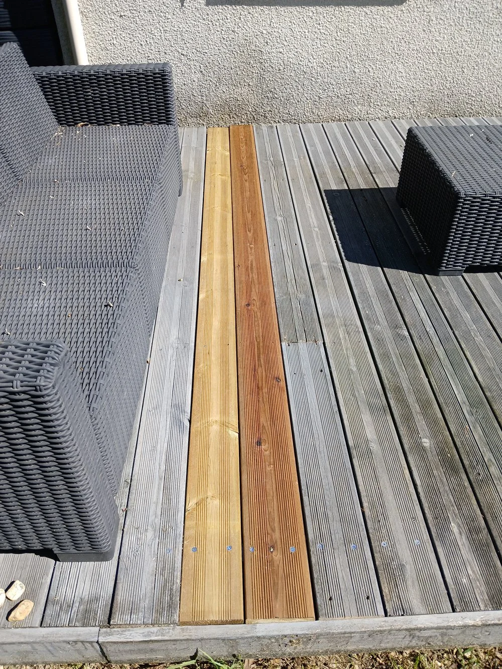 Terrasse avec deux fauteuils en résine tressée grise et deux petites tables en résine tressée, sol en bois avec une section de planches en différentes teintes de bois.