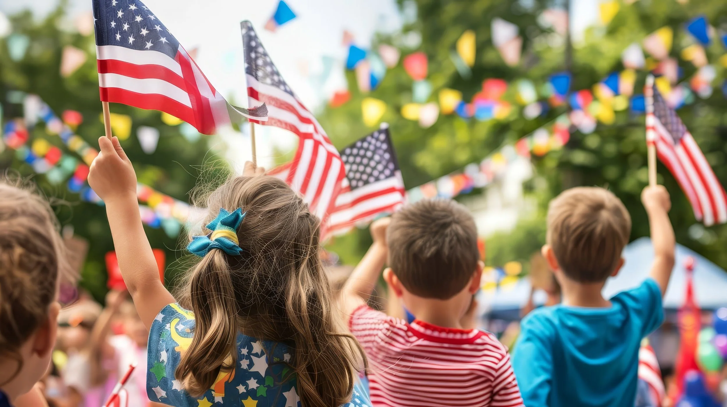 Children holding American flags at a celebration with colorful bunting in the background.