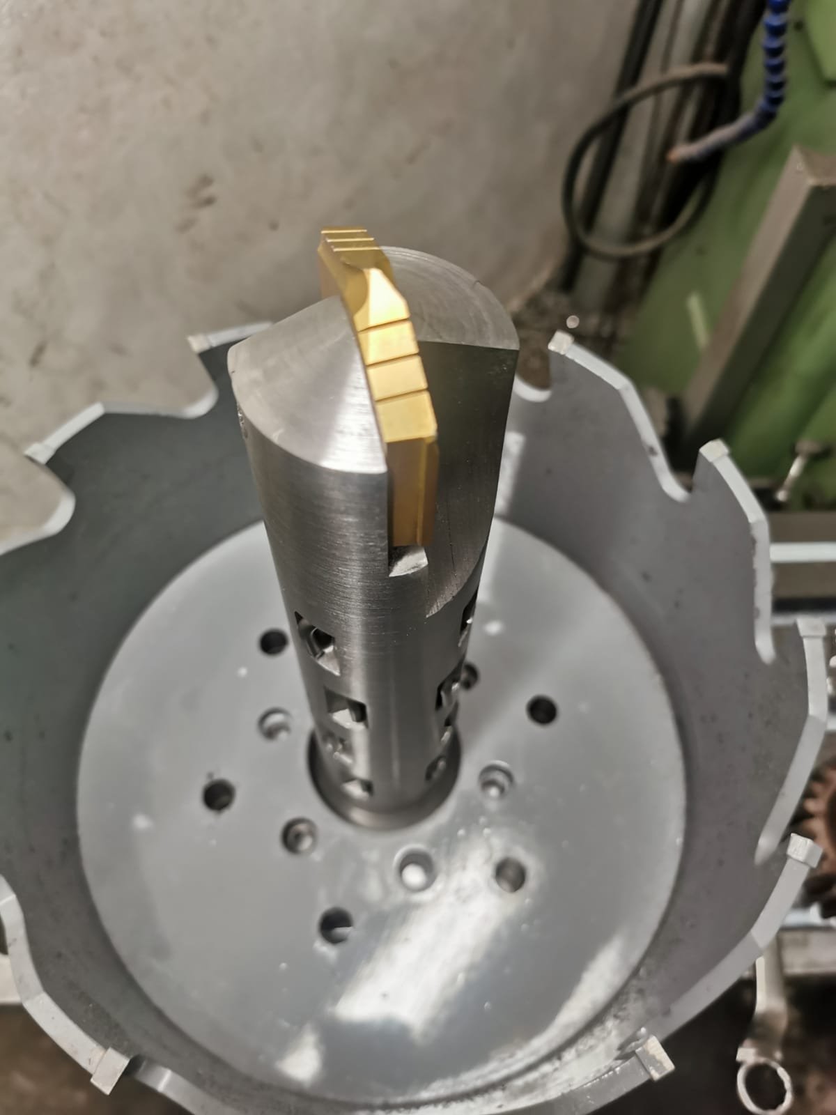 A metallic precision-machined component with gold-colored segments on top, set in a circular fixture, likely for manufacturing or engineering purposes.