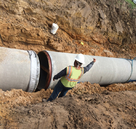 Construction worker installing a large concrete pipe in a trench.
