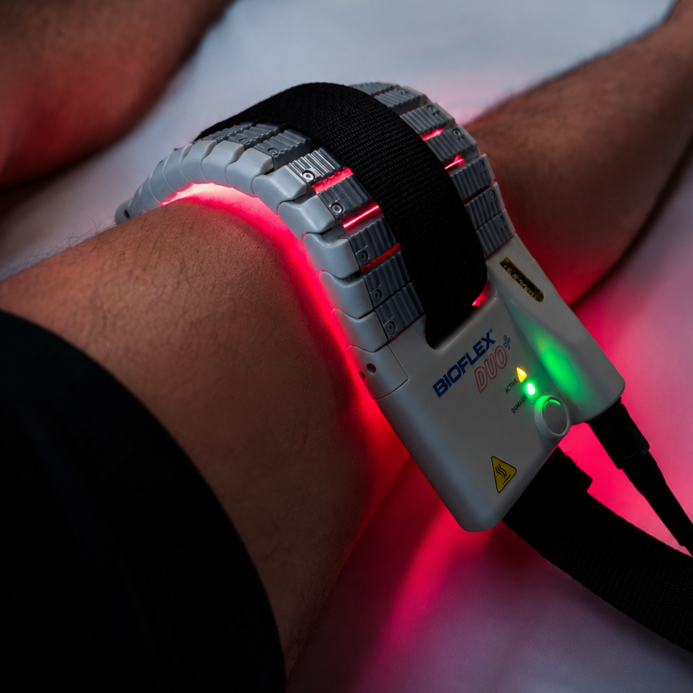 A person's arm has a medical device called BioFLEX DUO attached, which is emitting red lights and is secured with a black strap.
