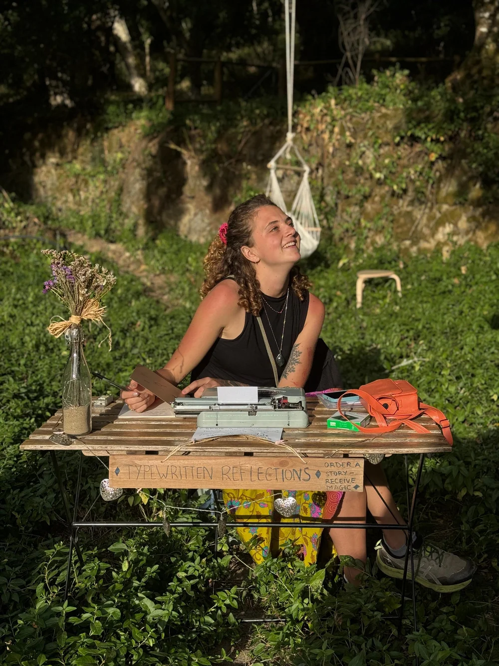 Julie writing at her typewriter at a wooden table outdoors