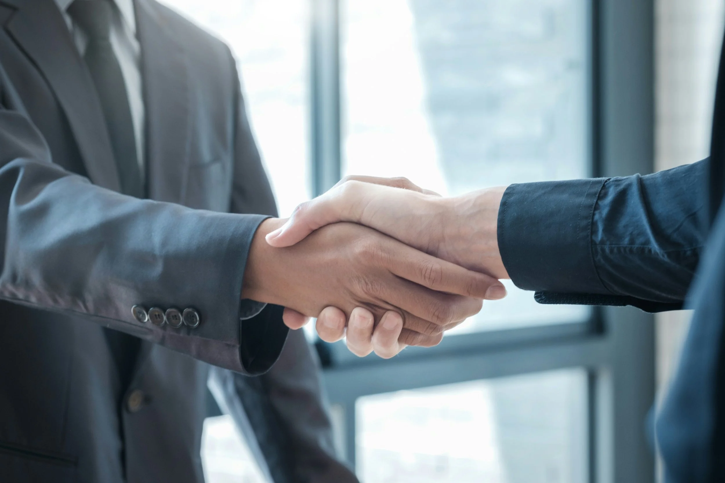 Two individuals in business attire shaking hands in a modern office setting.